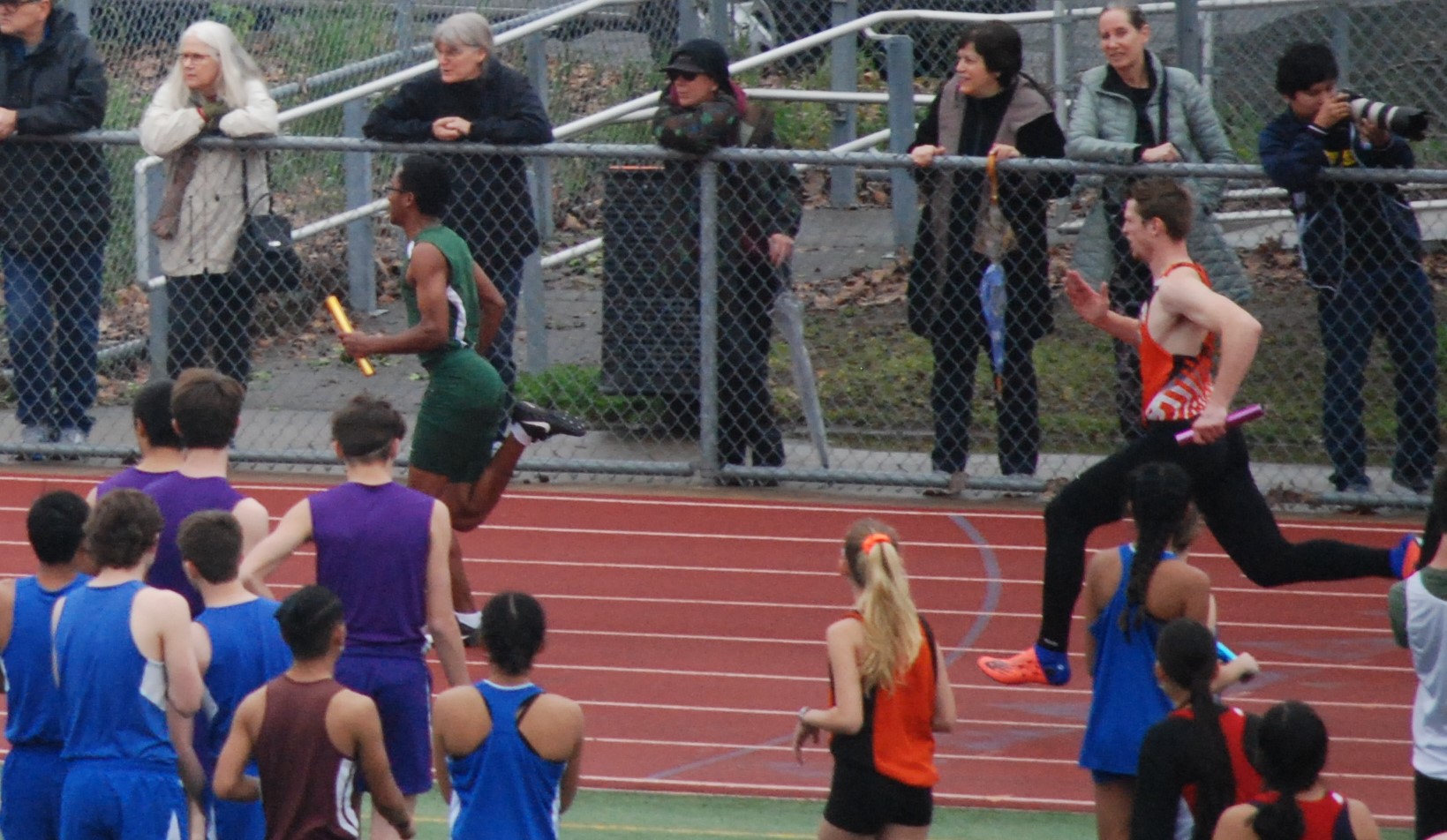 Athlete prepares for pole vault on a track with others watching.