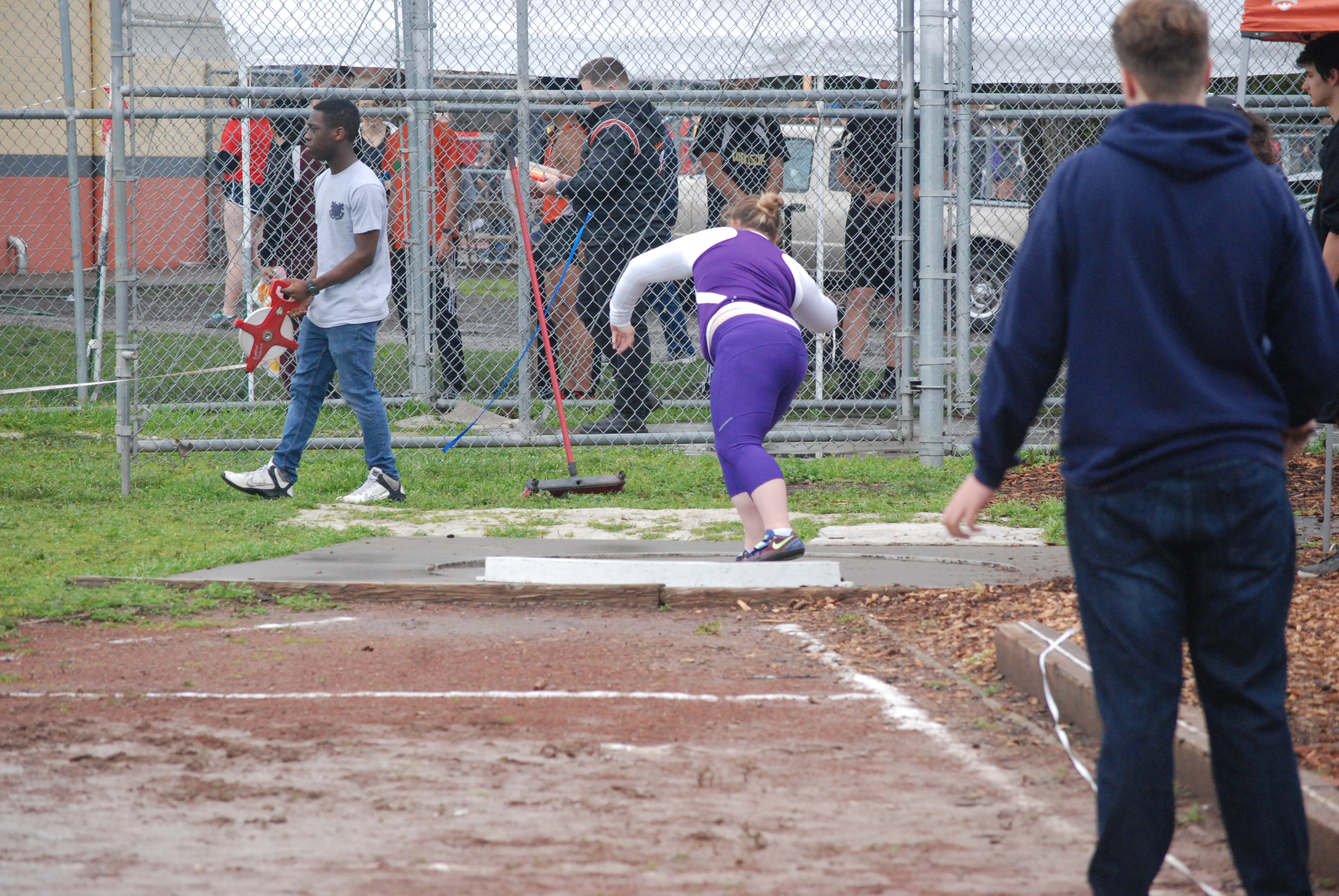 Athlete prepares for pole vault on a track with others watching.