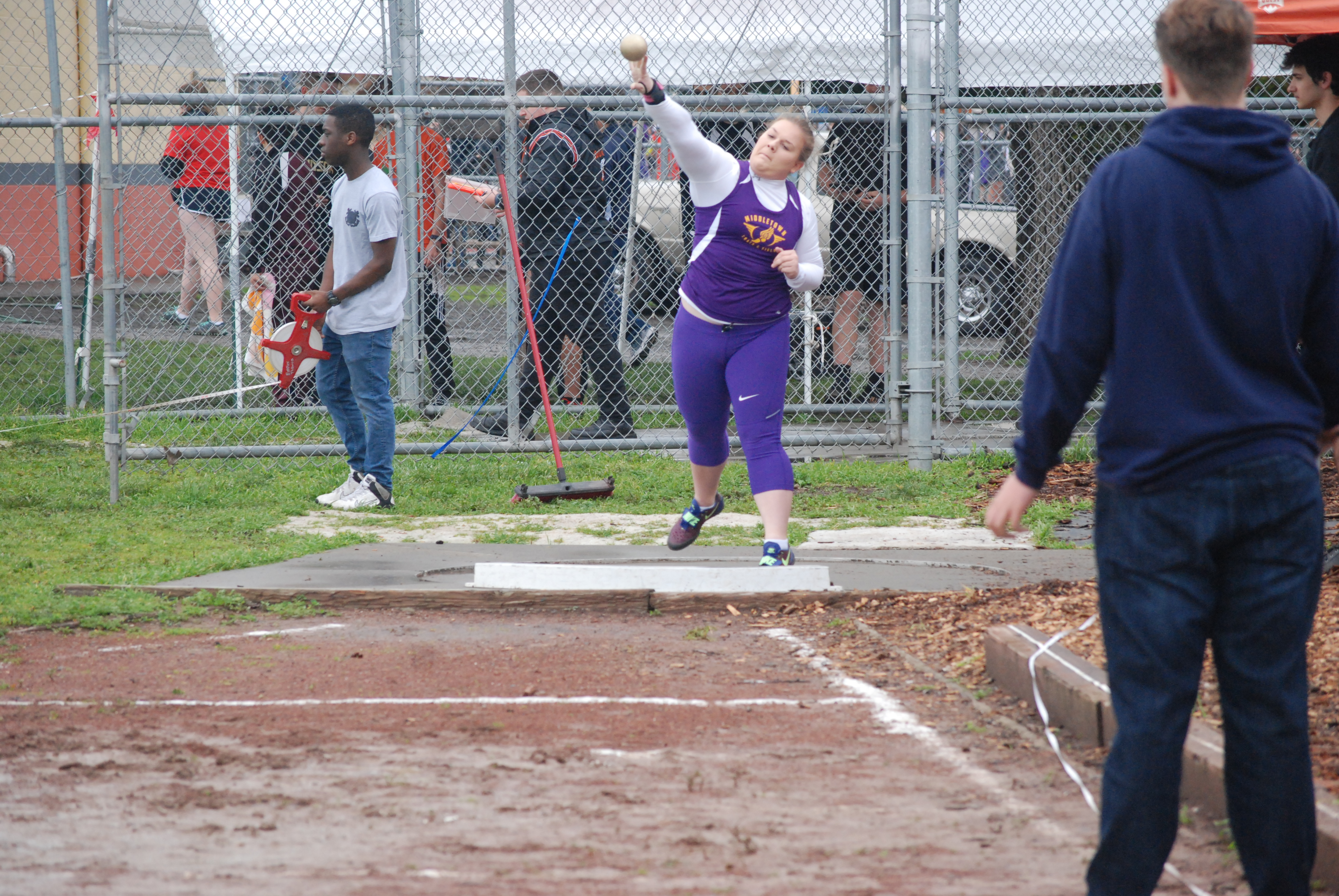 Athlete prepares for pole vault on a track with others watching.