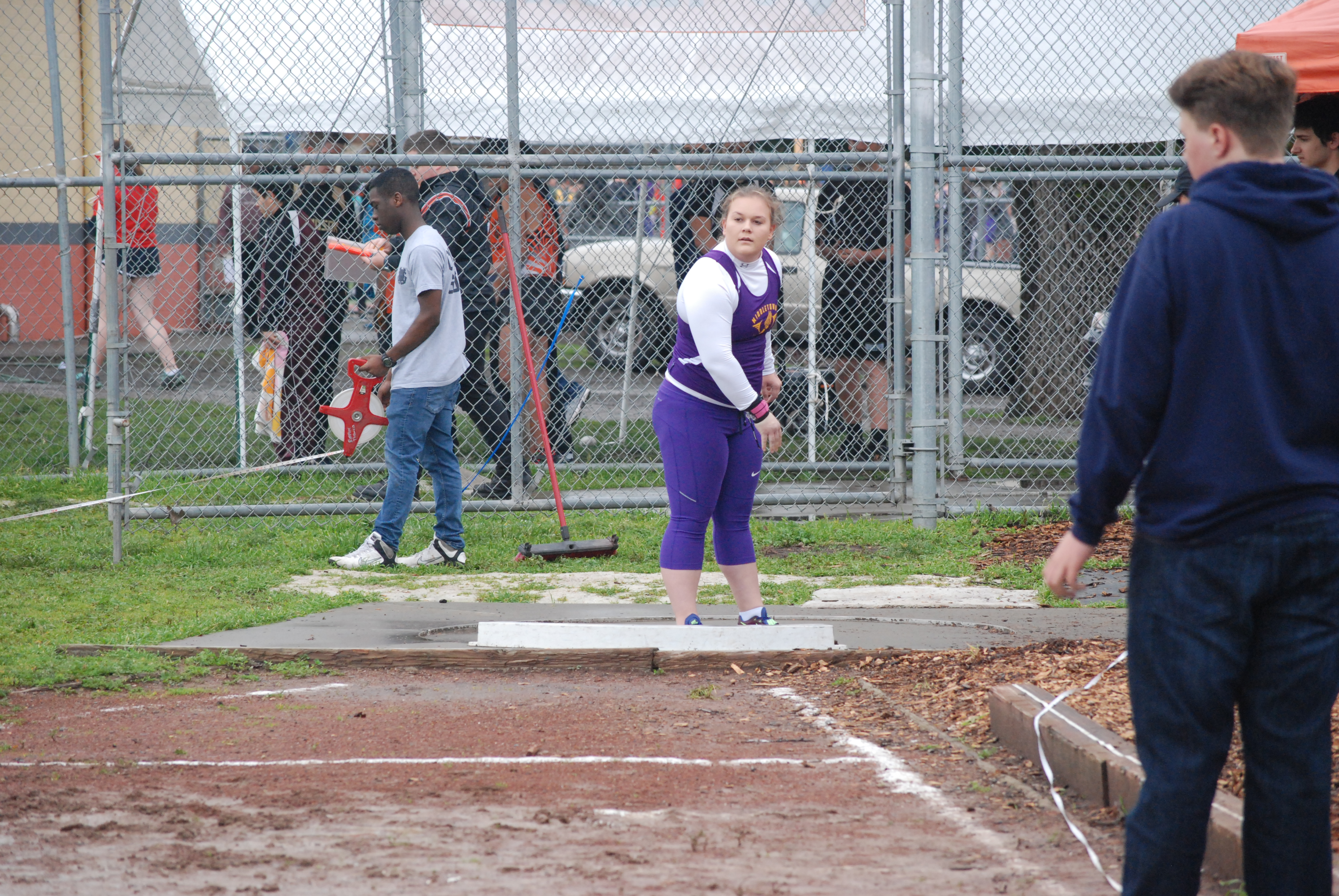 Athlete prepares for pole vault on a track with others watching.