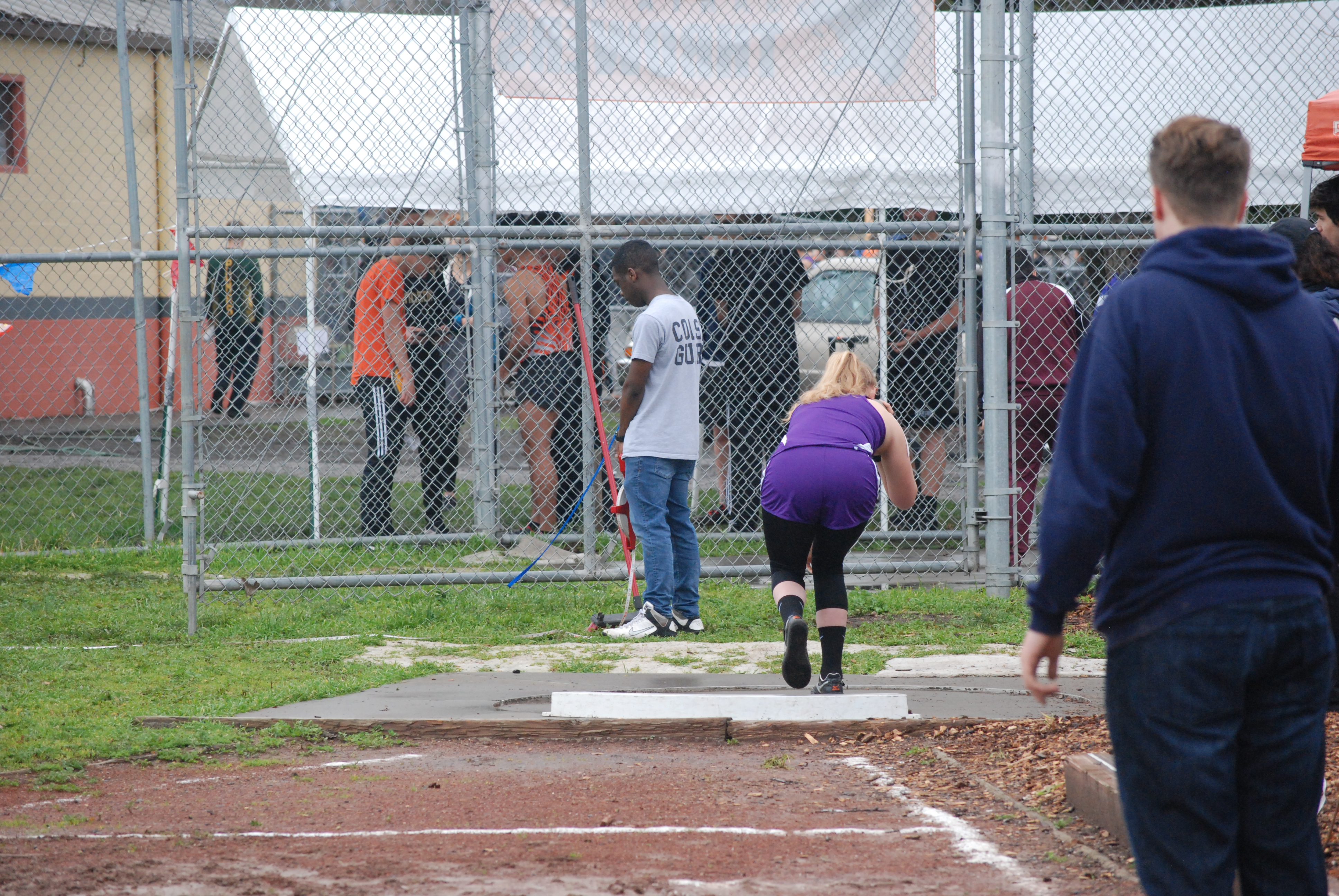 Athlete prepares for pole vault on a track with others watching.