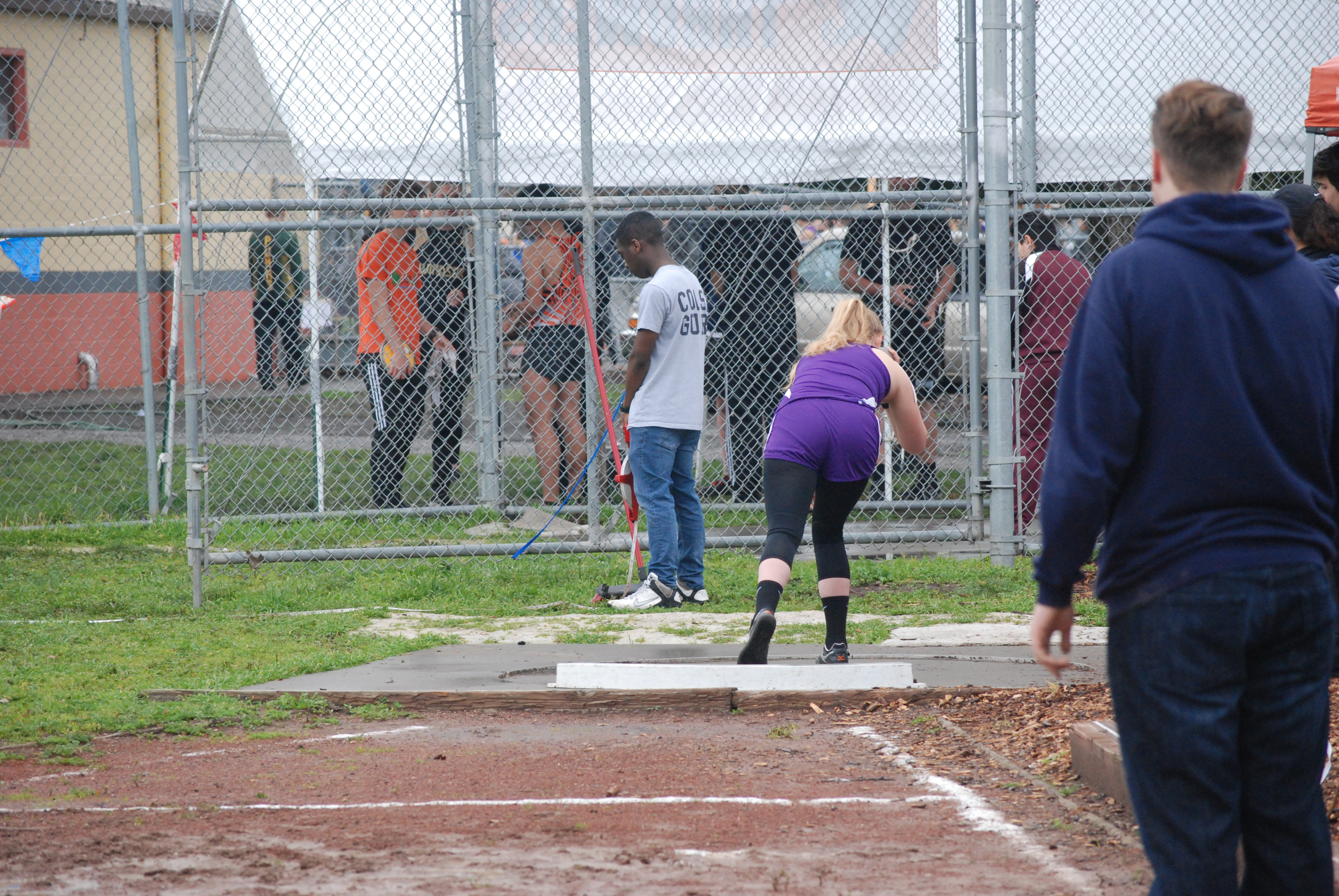 Athlete prepares for pole vault on a track with others watching.