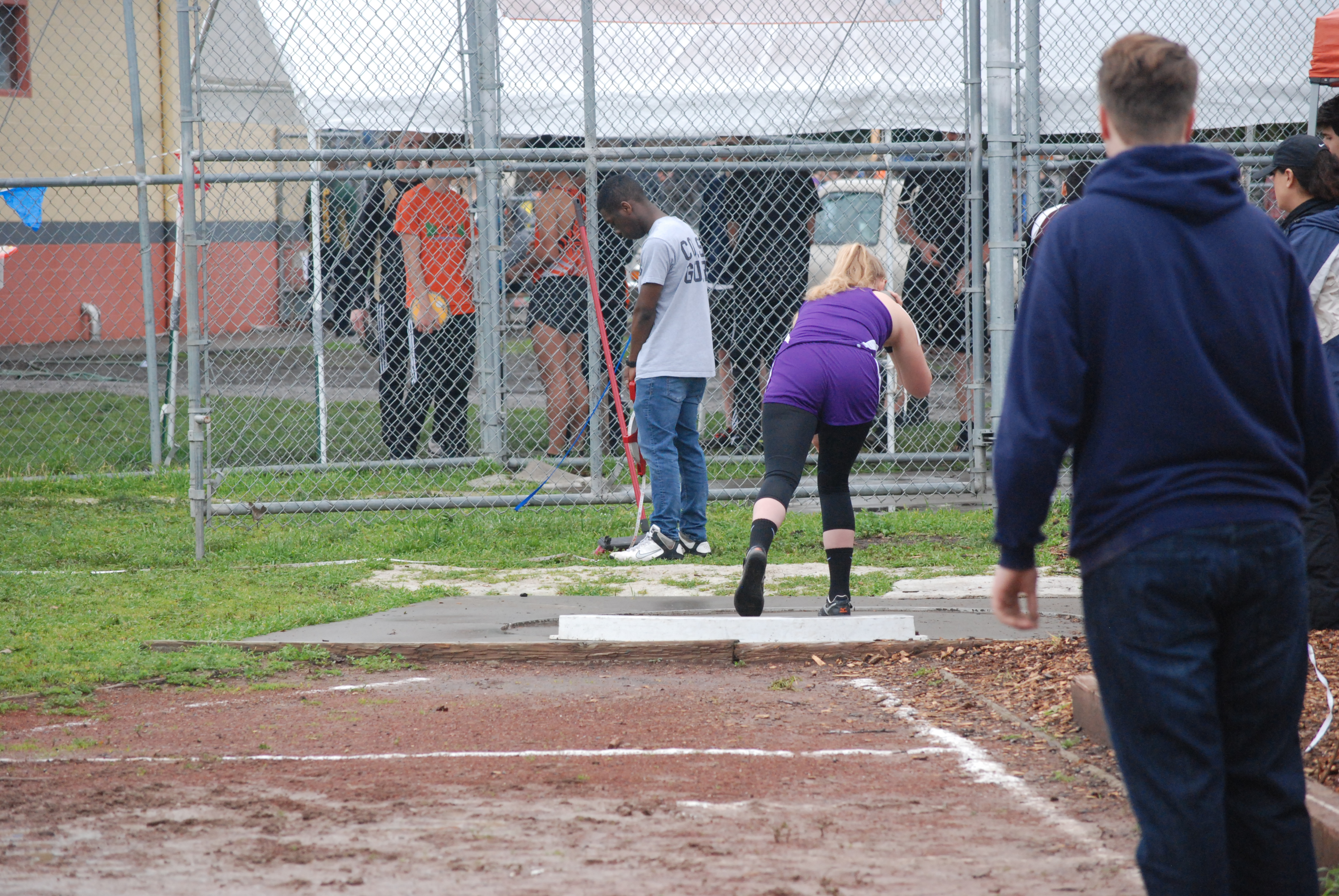 Athlete prepares for pole vault on a track with others watching.