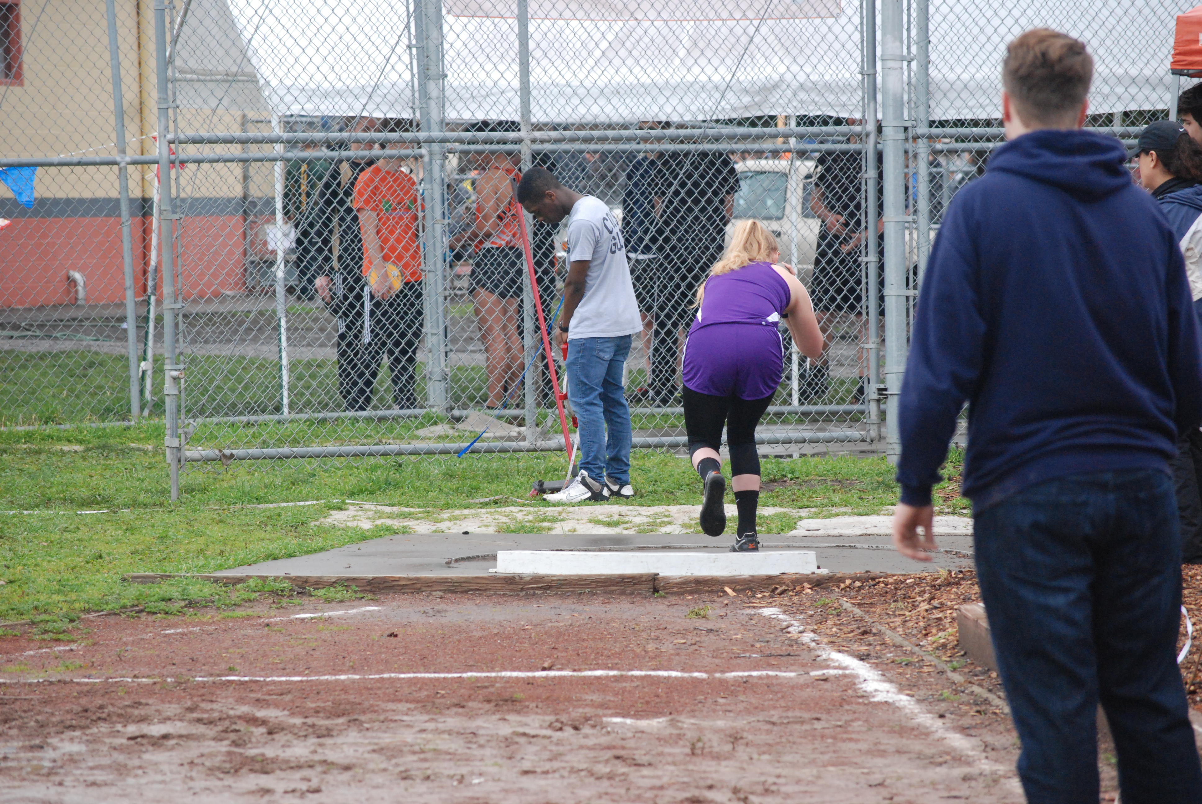 Athlete prepares for pole vault on a track with others watching.
