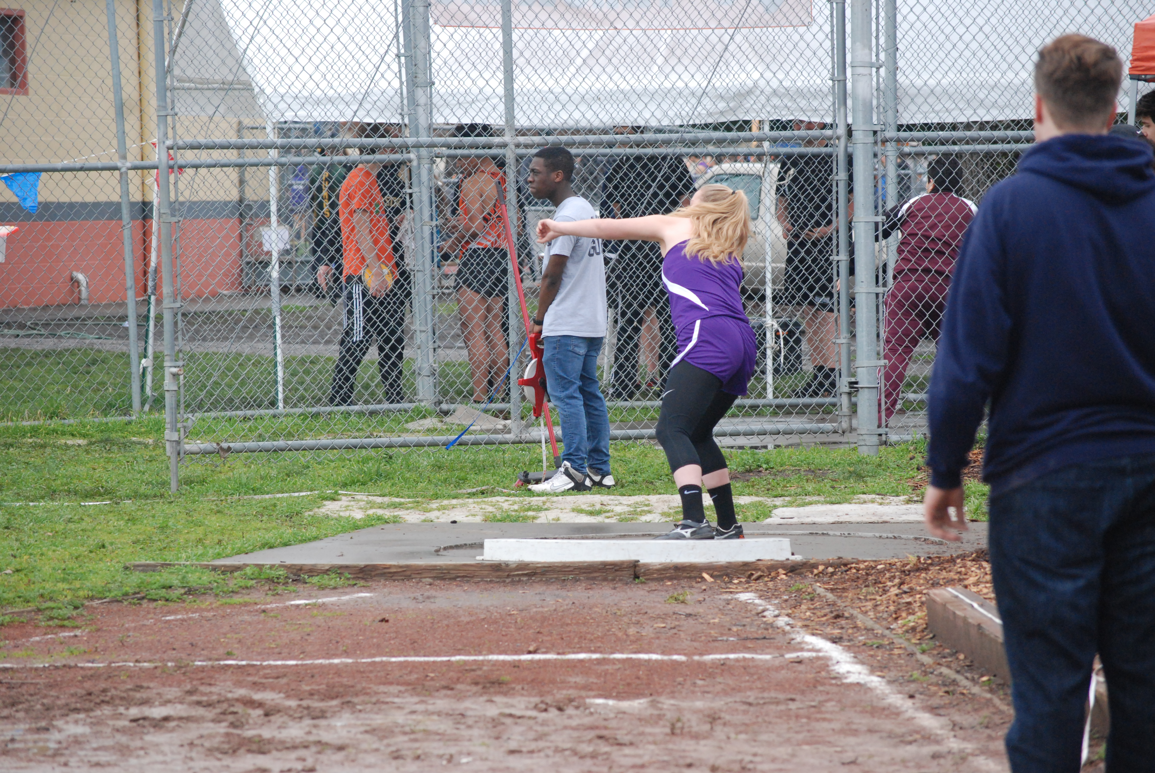 Athlete prepares for pole vault on a track with others watching.