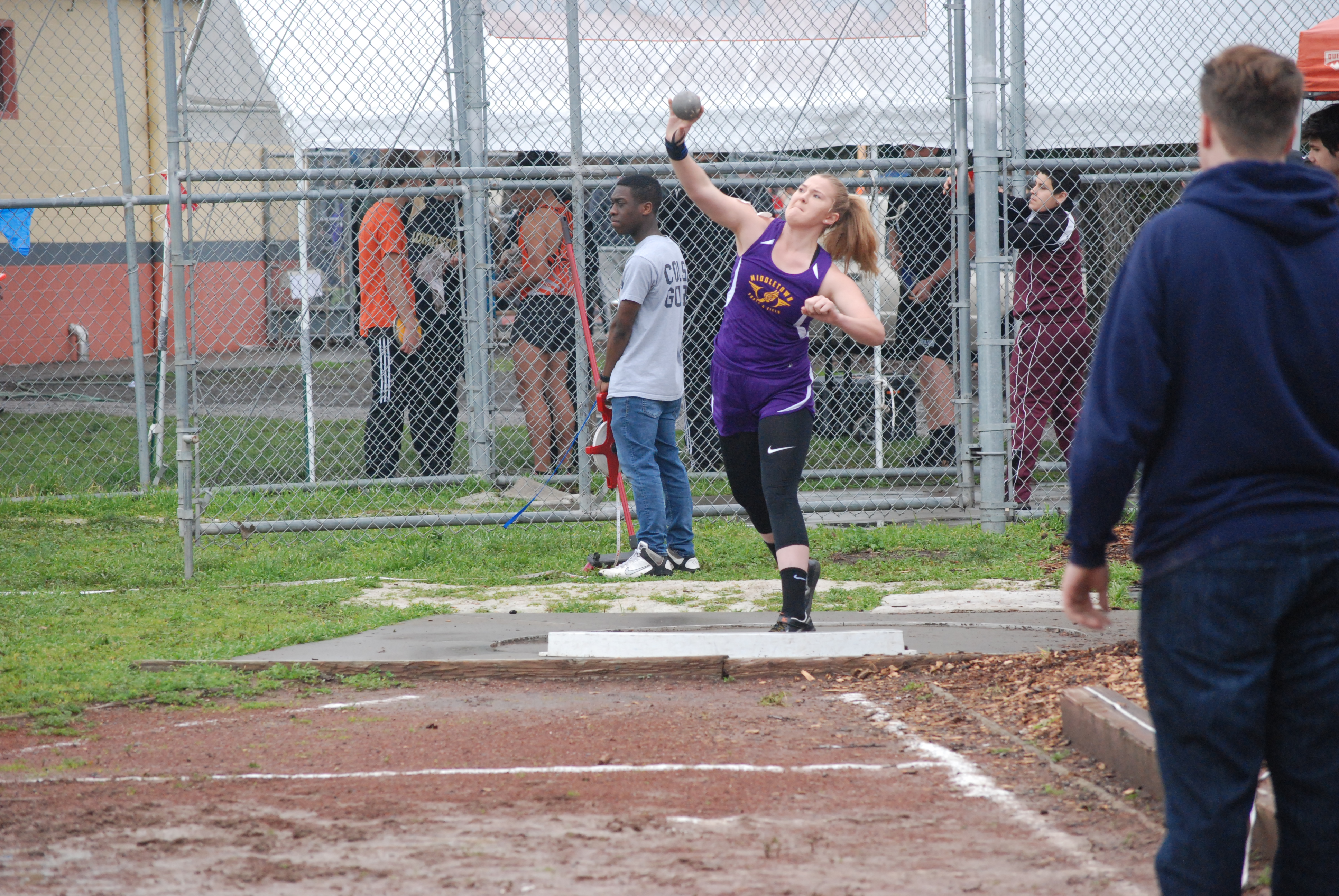 Athlete prepares for pole vault on a track with others watching.