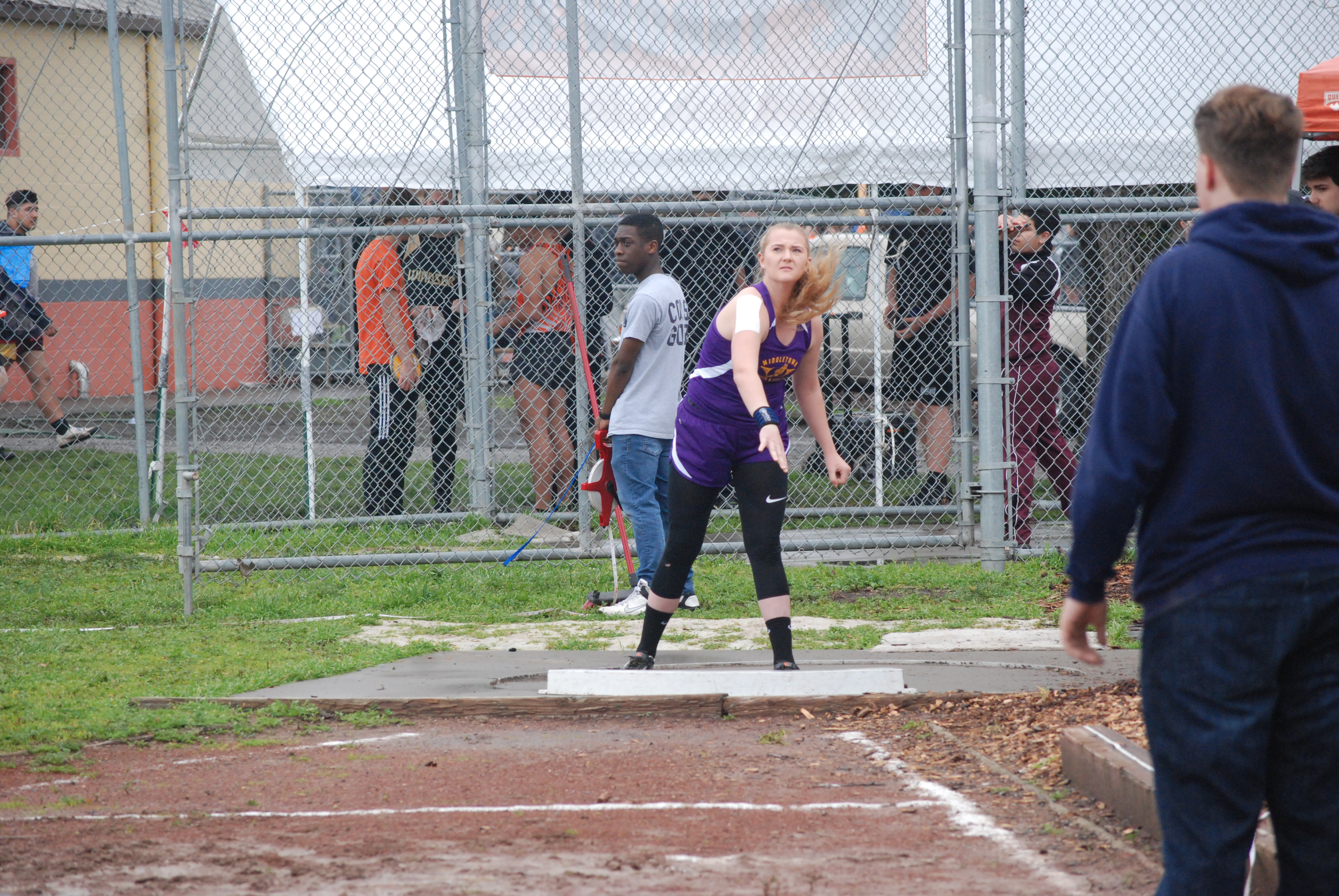Athlete prepares for pole vault on a track with others watching.