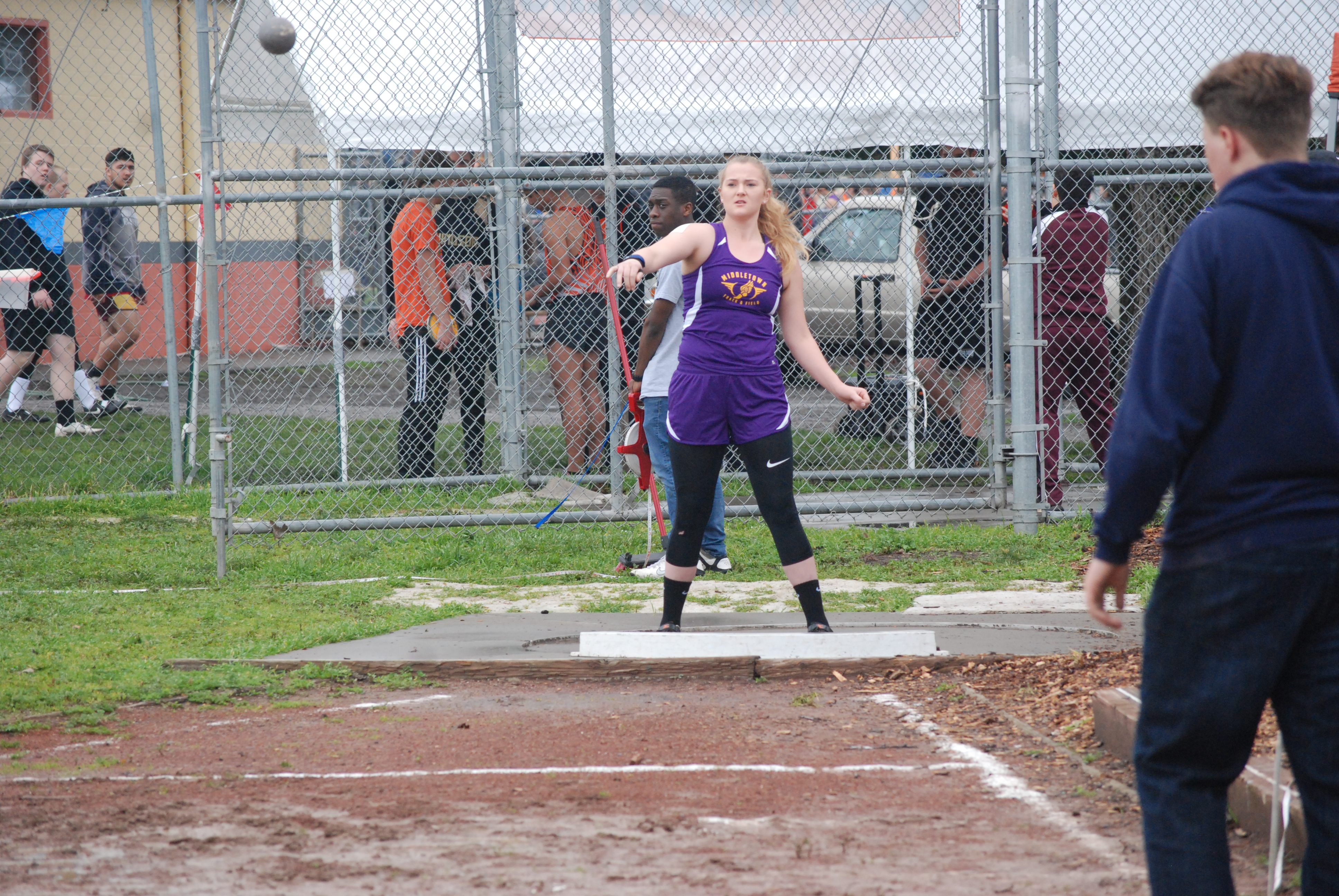 Athlete prepares for pole vault on a track with others watching.