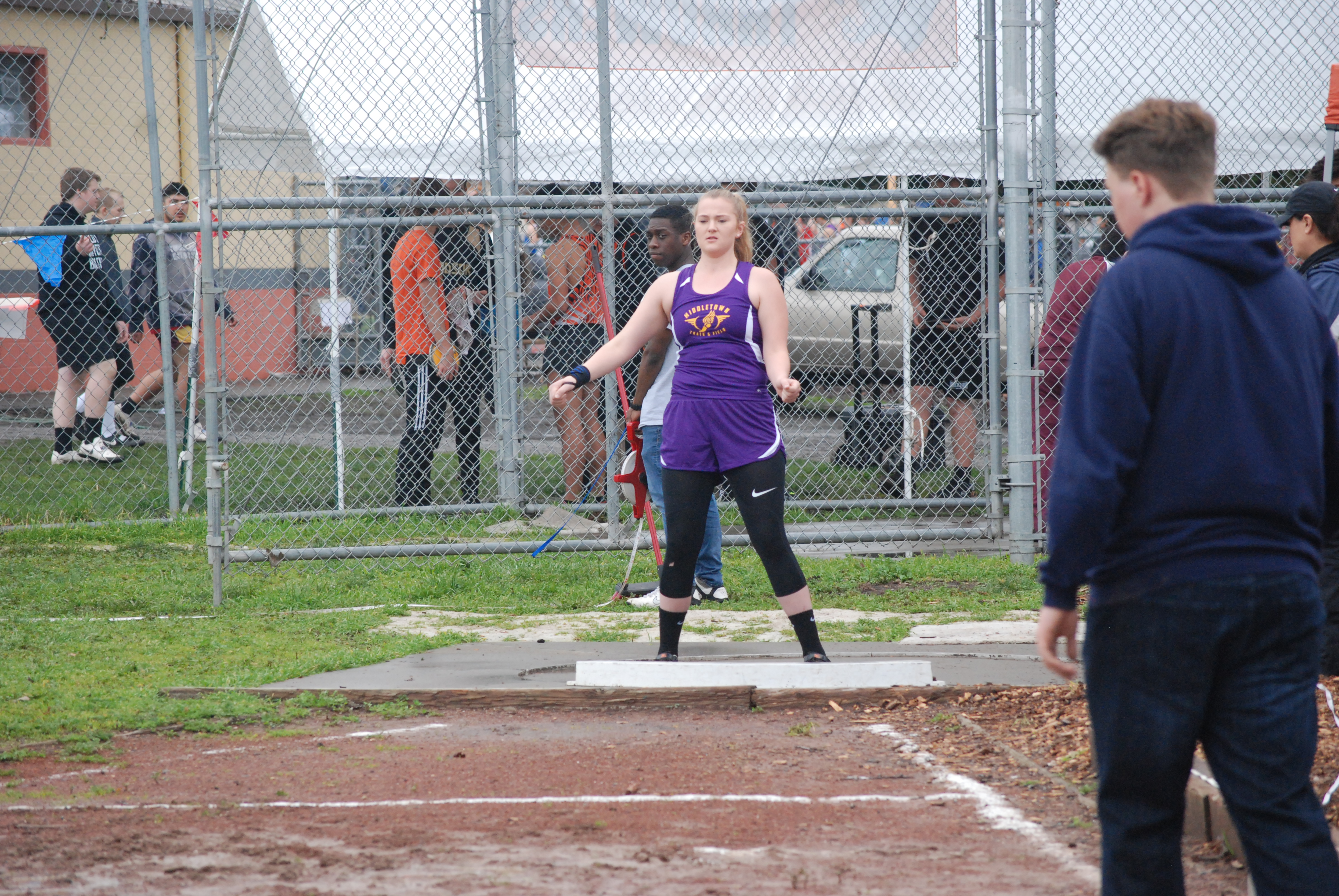 Athlete prepares for pole vault on a track with others watching.