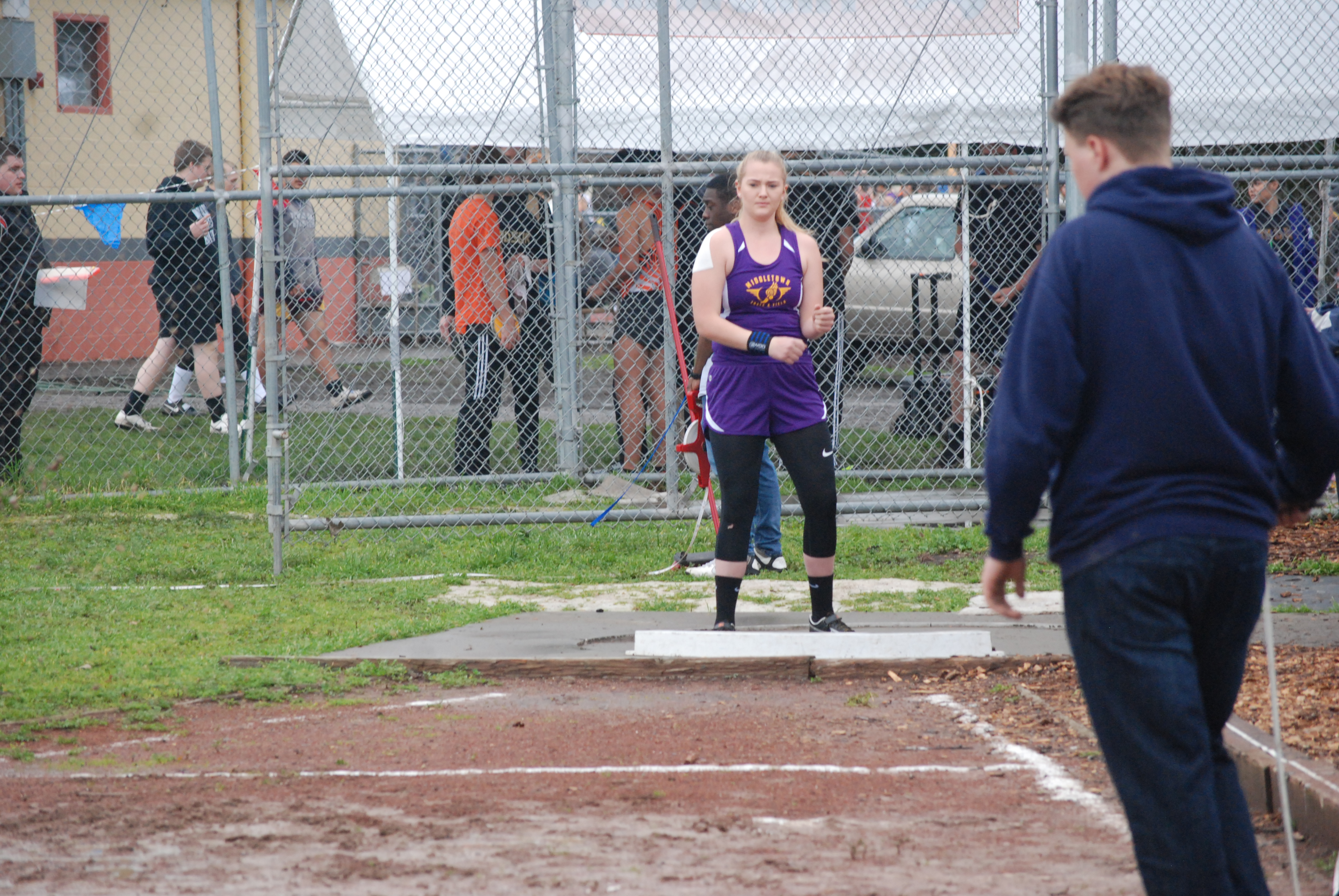 Athlete prepares for pole vault on a track with others watching.