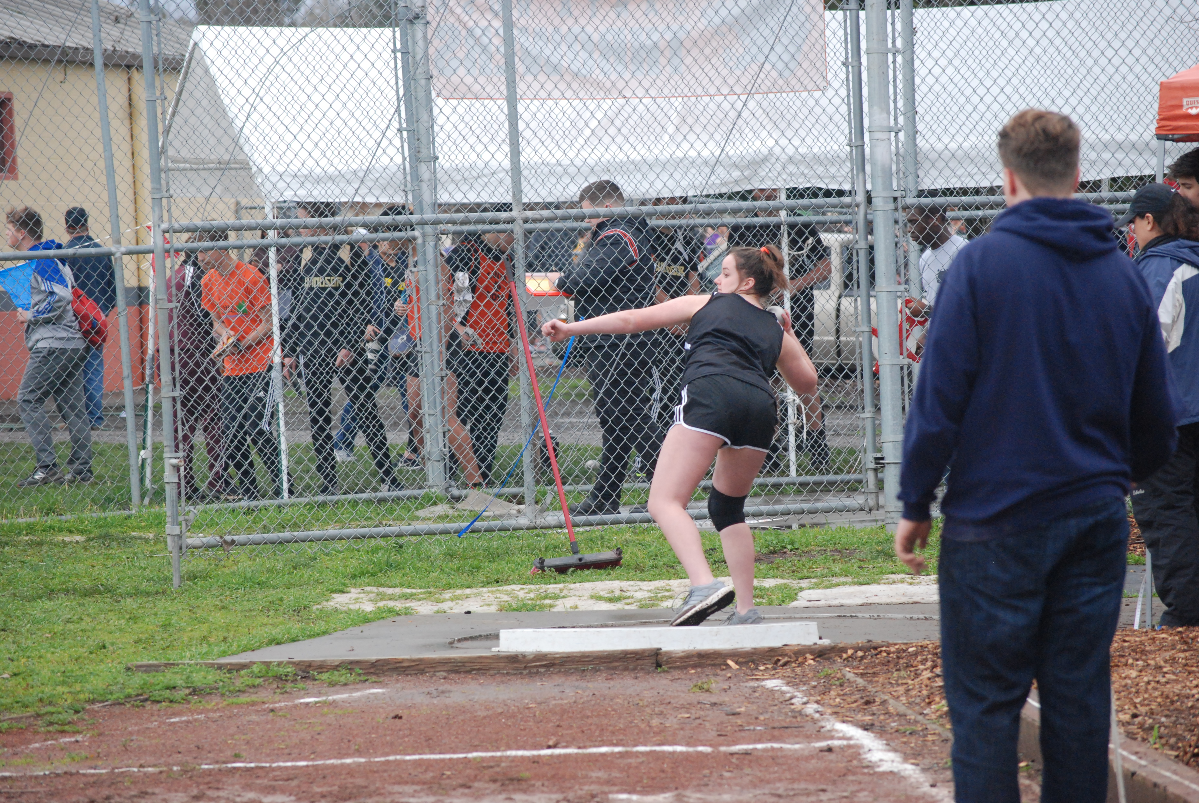 Athlete prepares for pole vault on a track with others watching.