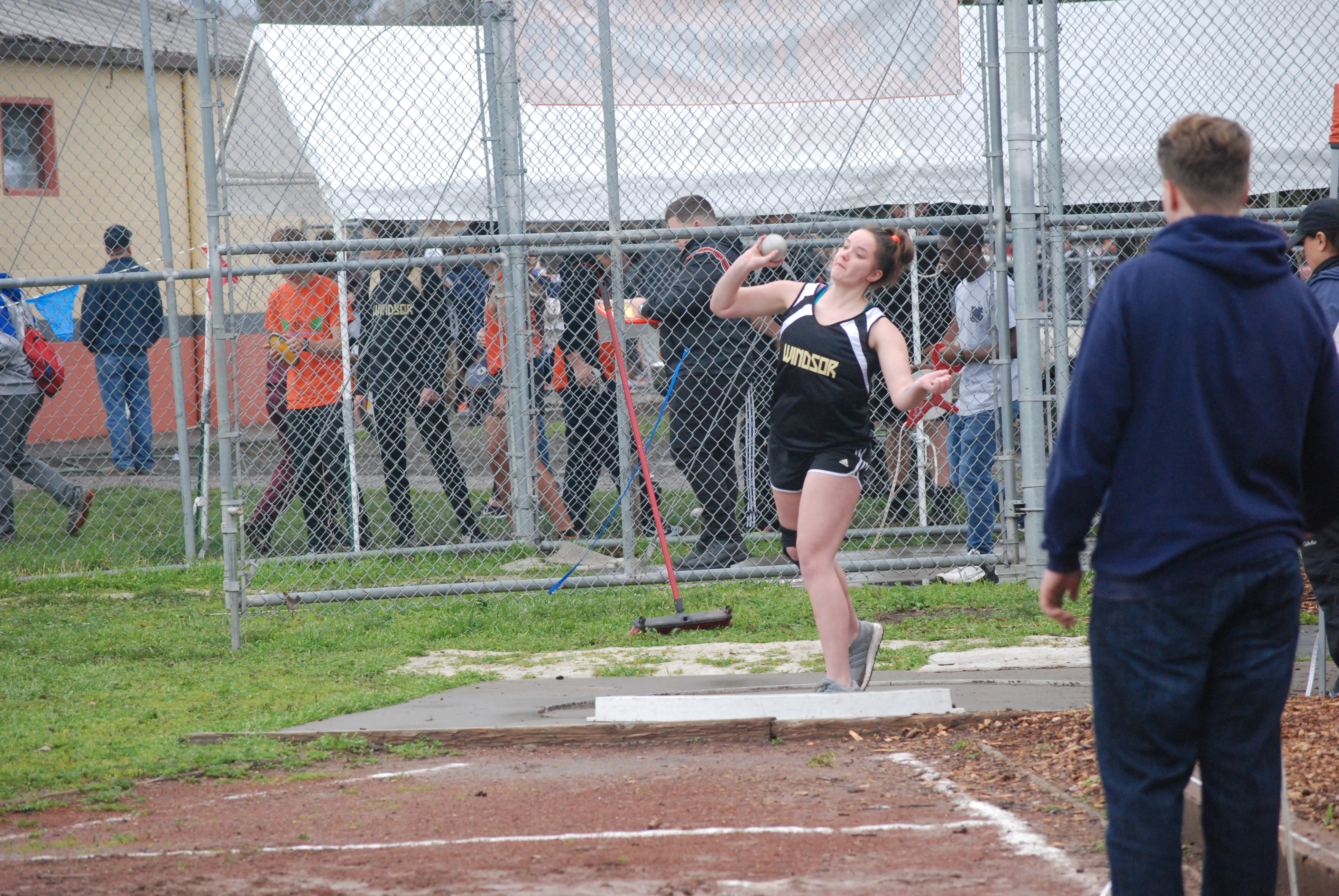 Athlete prepares for pole vault on a track with others watching.