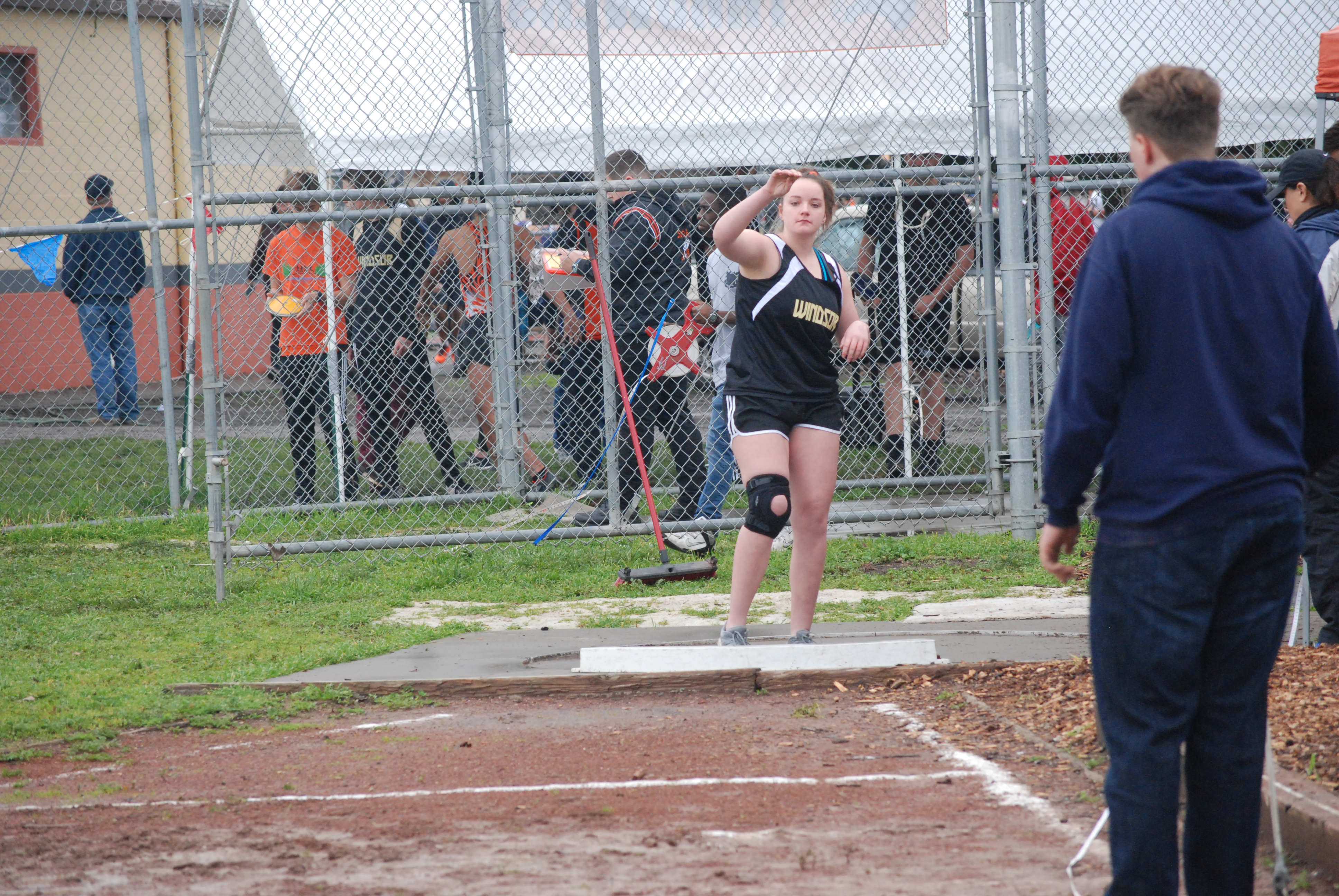 Athlete prepares for pole vault on a track with others watching.