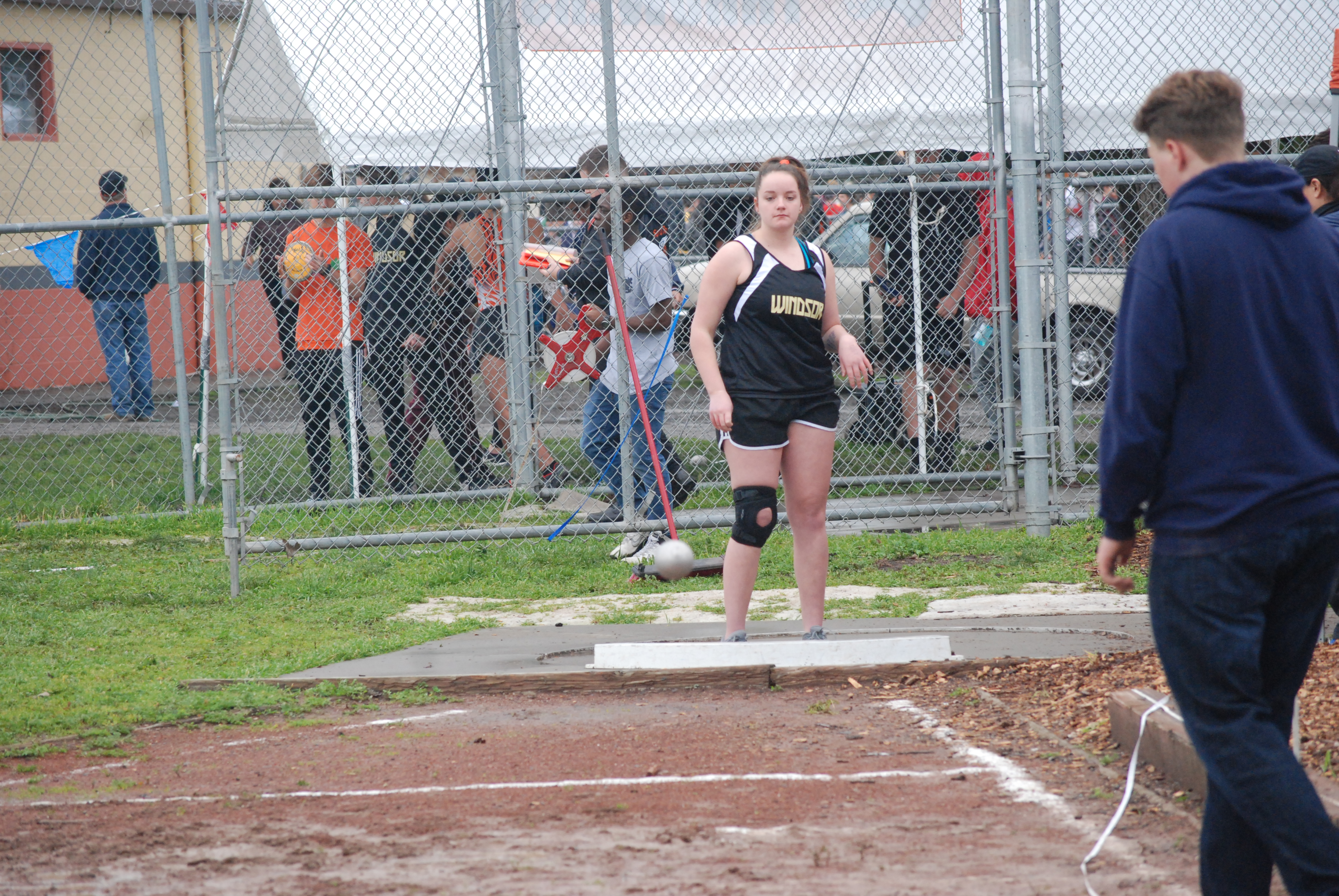 Athlete prepares for pole vault on a track with others watching.