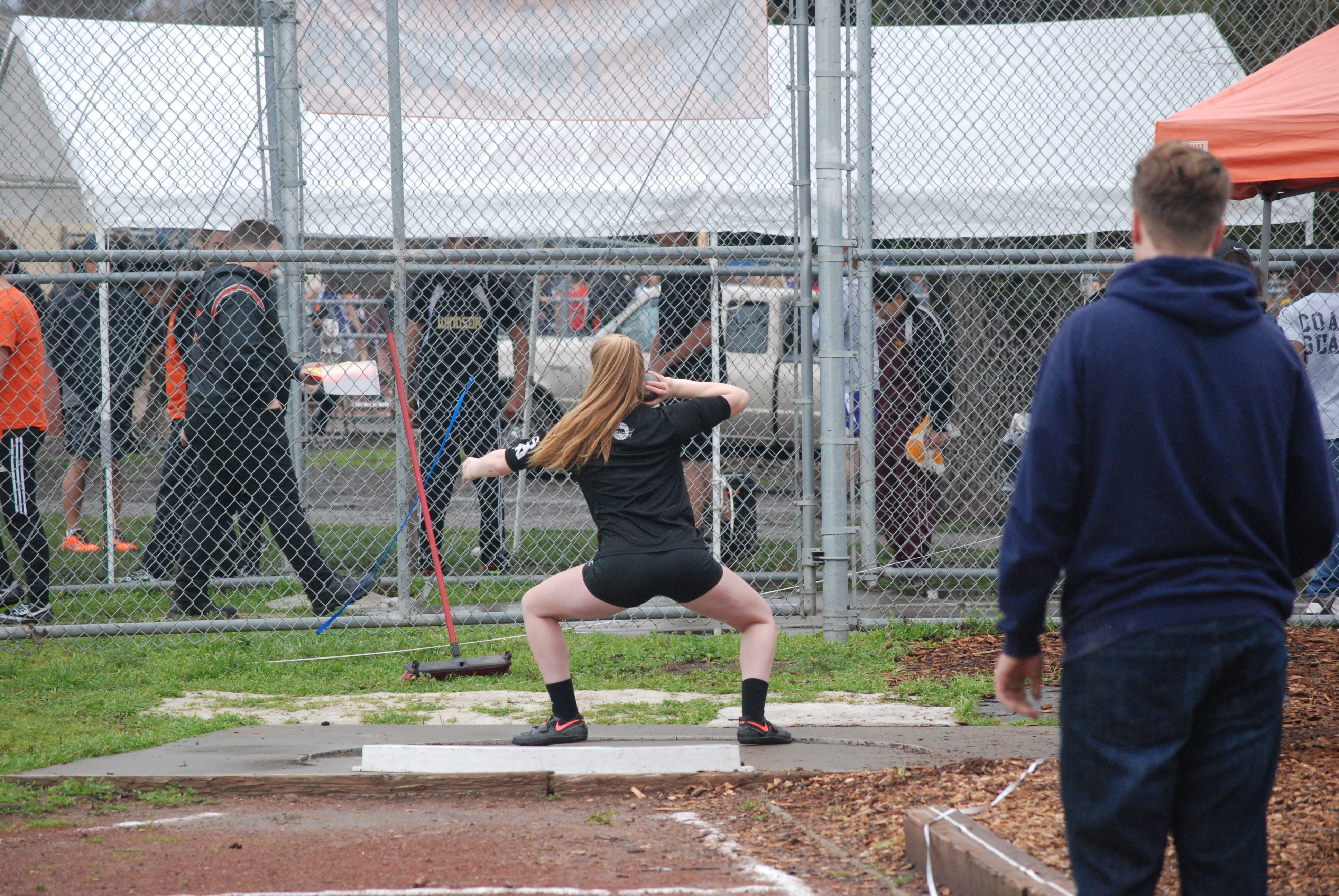 Athlete prepares for pole vault on a track with others watching.