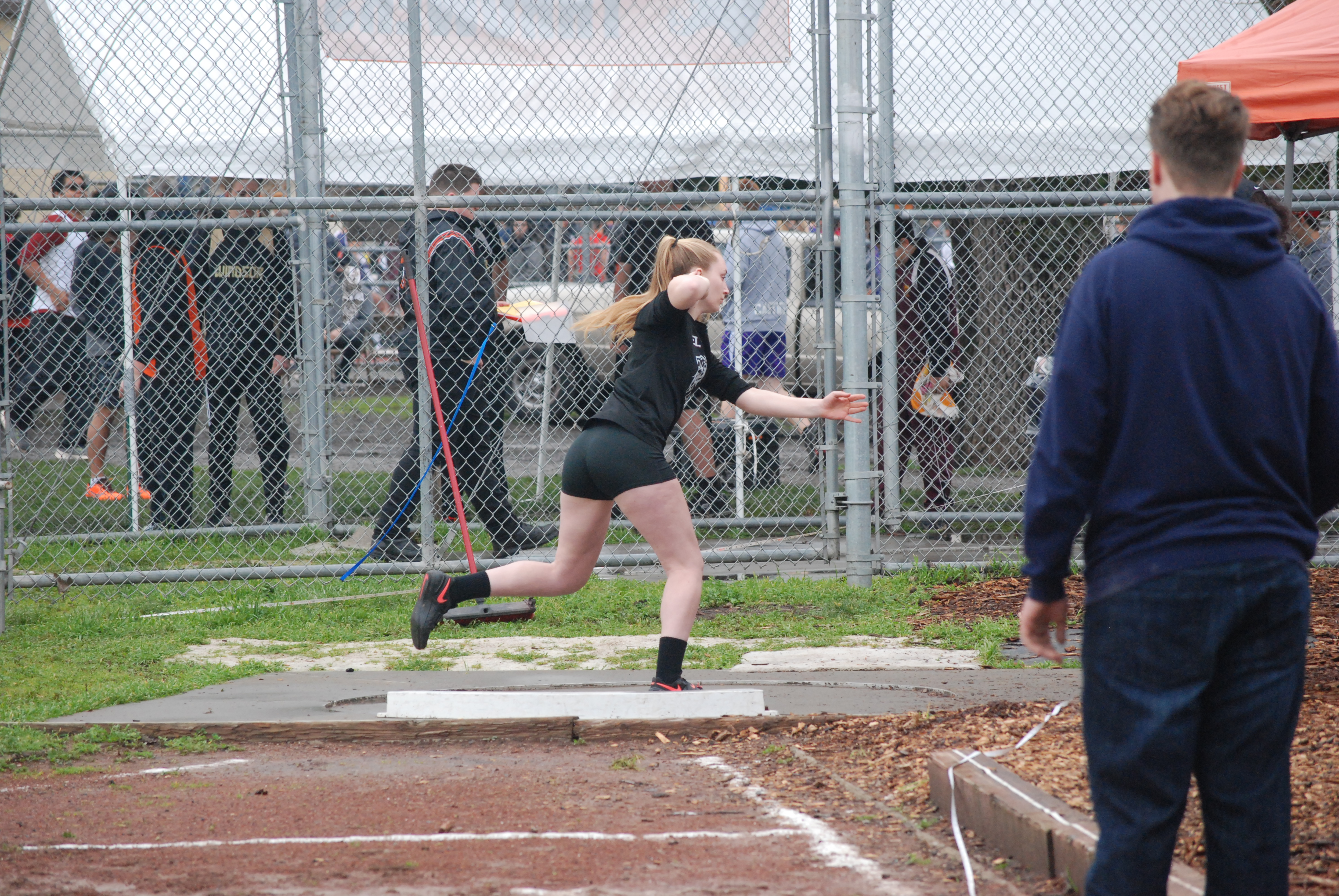 Athlete prepares for pole vault on a track with others watching.