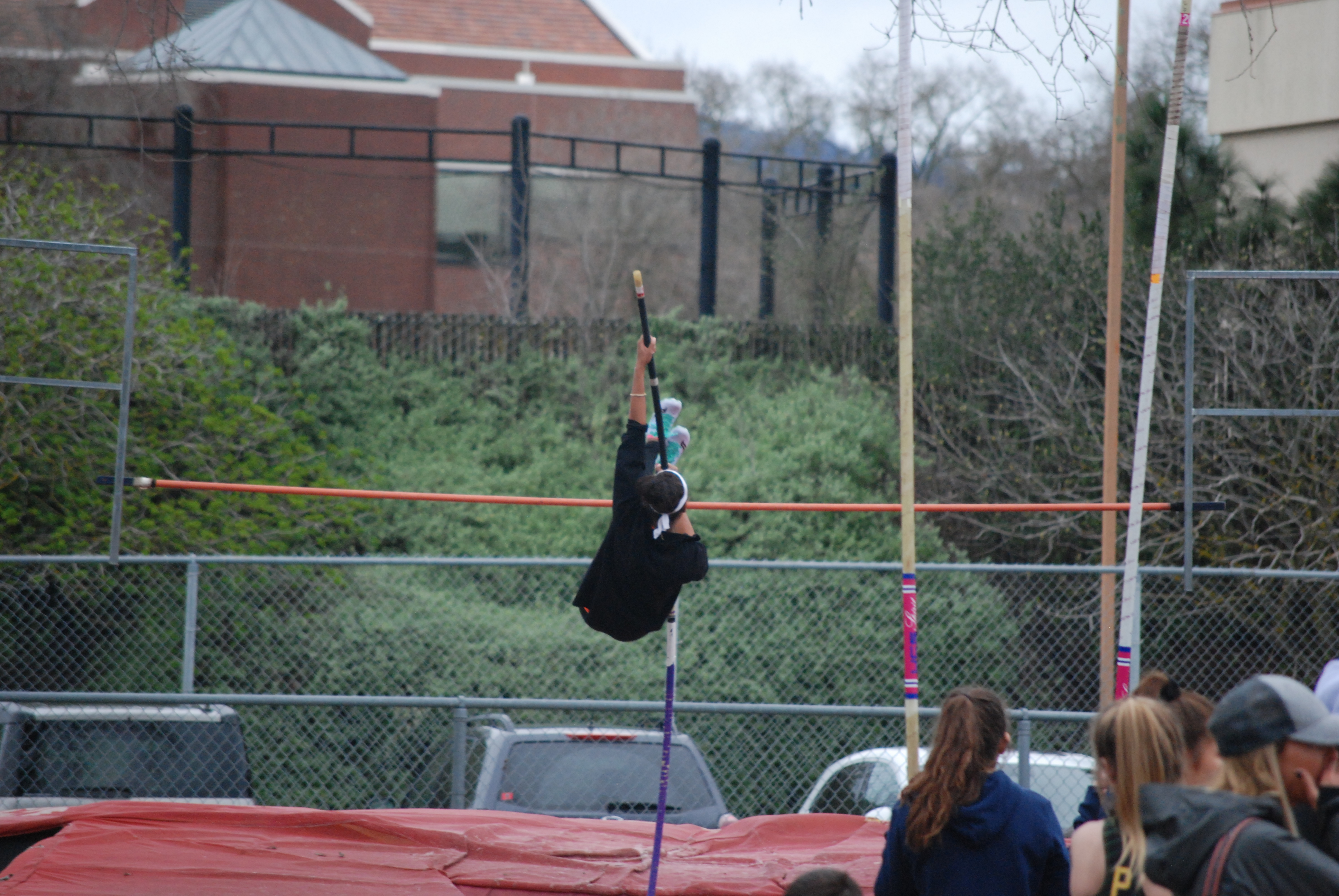 Athlete prepares for pole vault on a track with others watching.