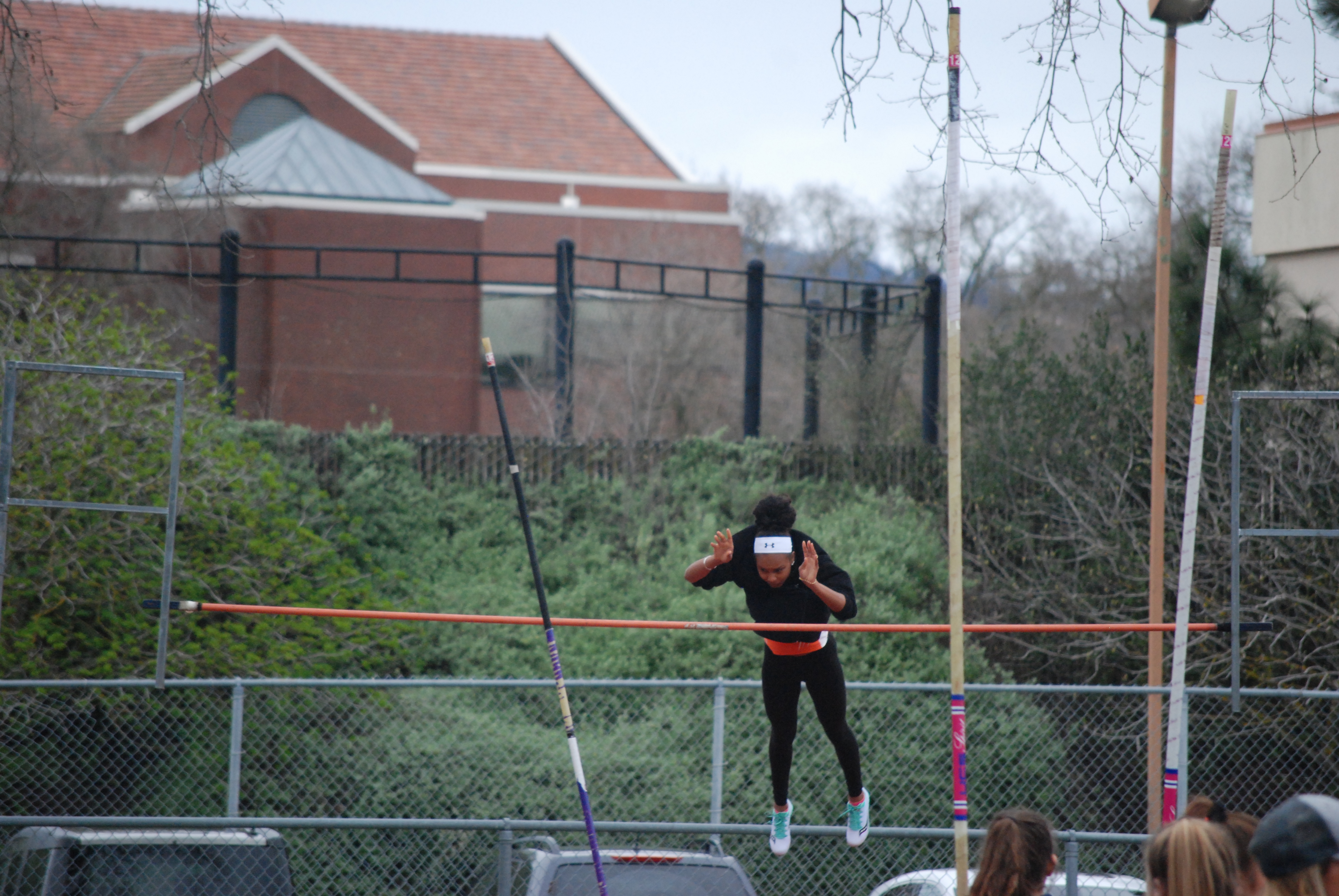 Athlete prepares for pole vault on a track with others watching.