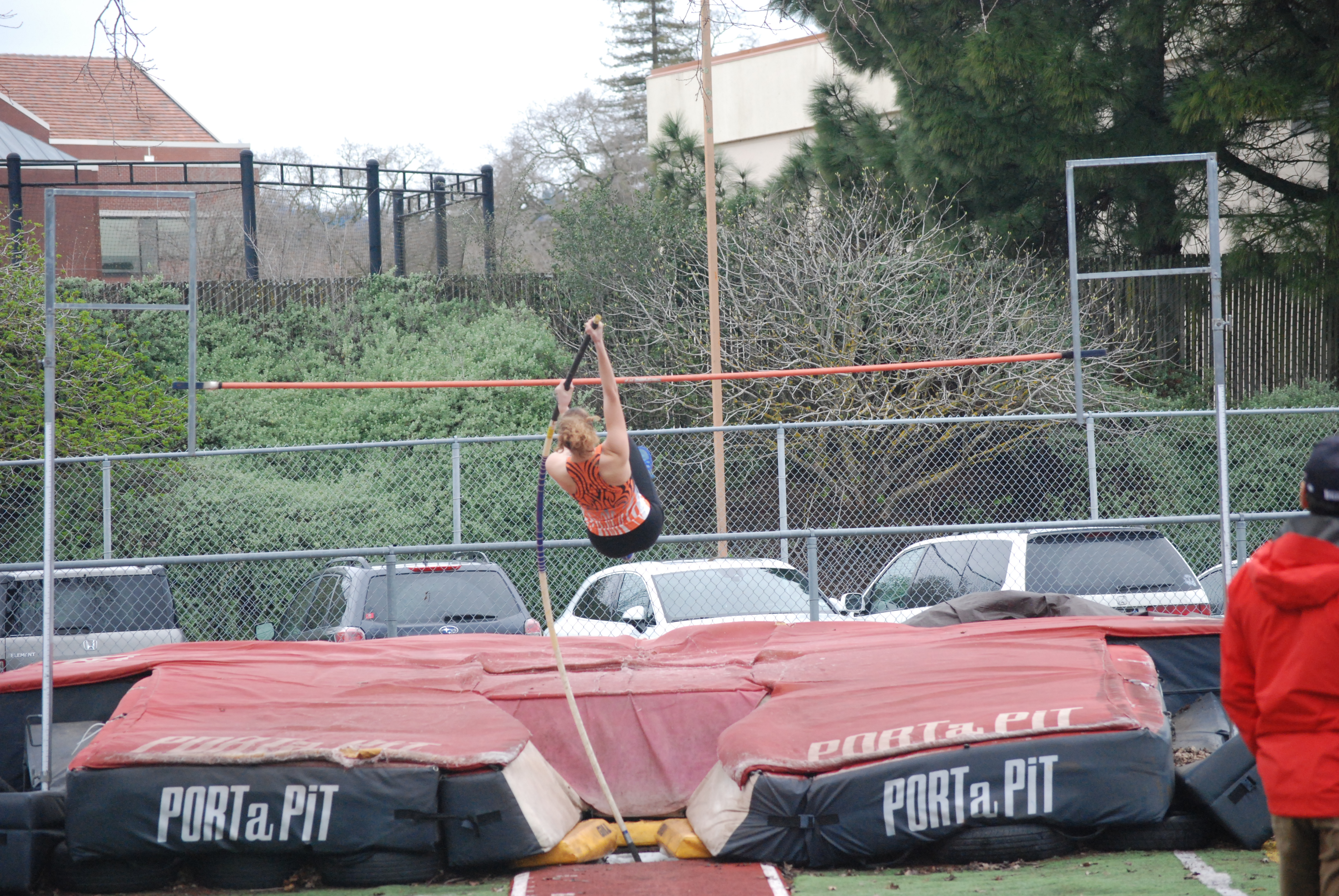 Athlete prepares for pole vault on a track with others watching.