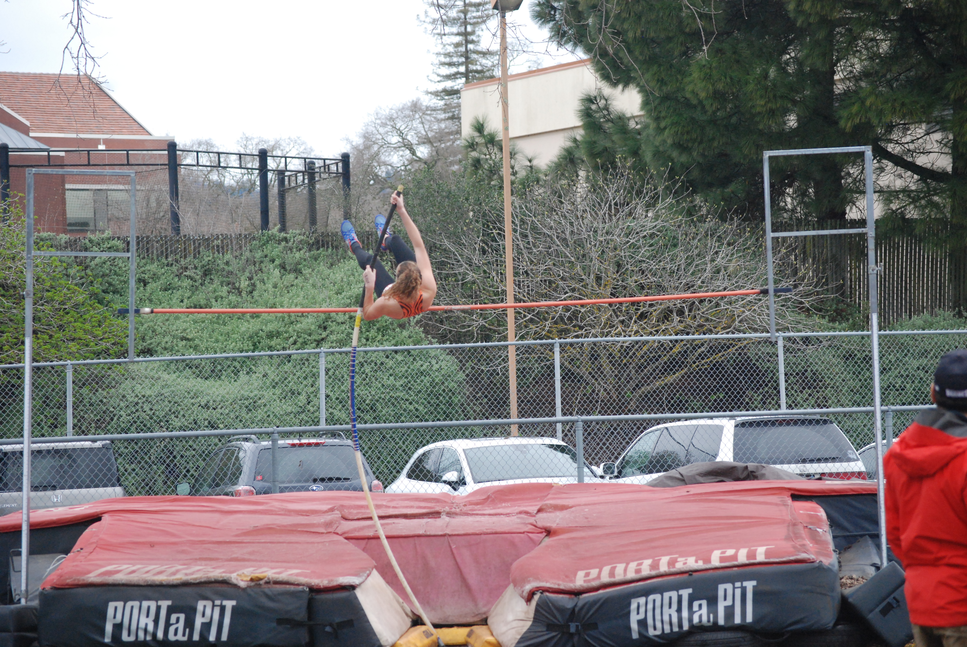 Athlete prepares for pole vault on a track with others watching.