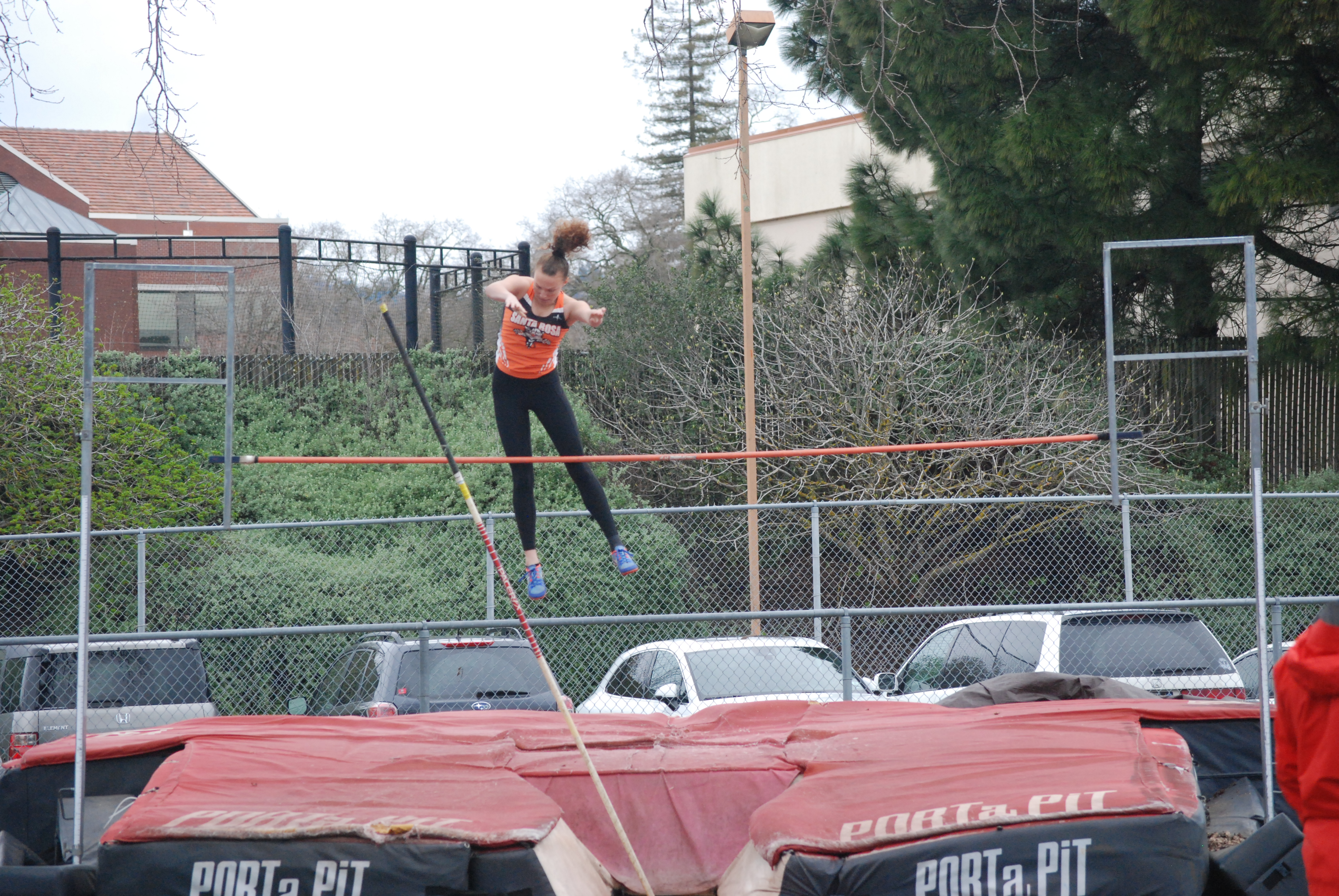 Athlete prepares for pole vault on a track with others watching.