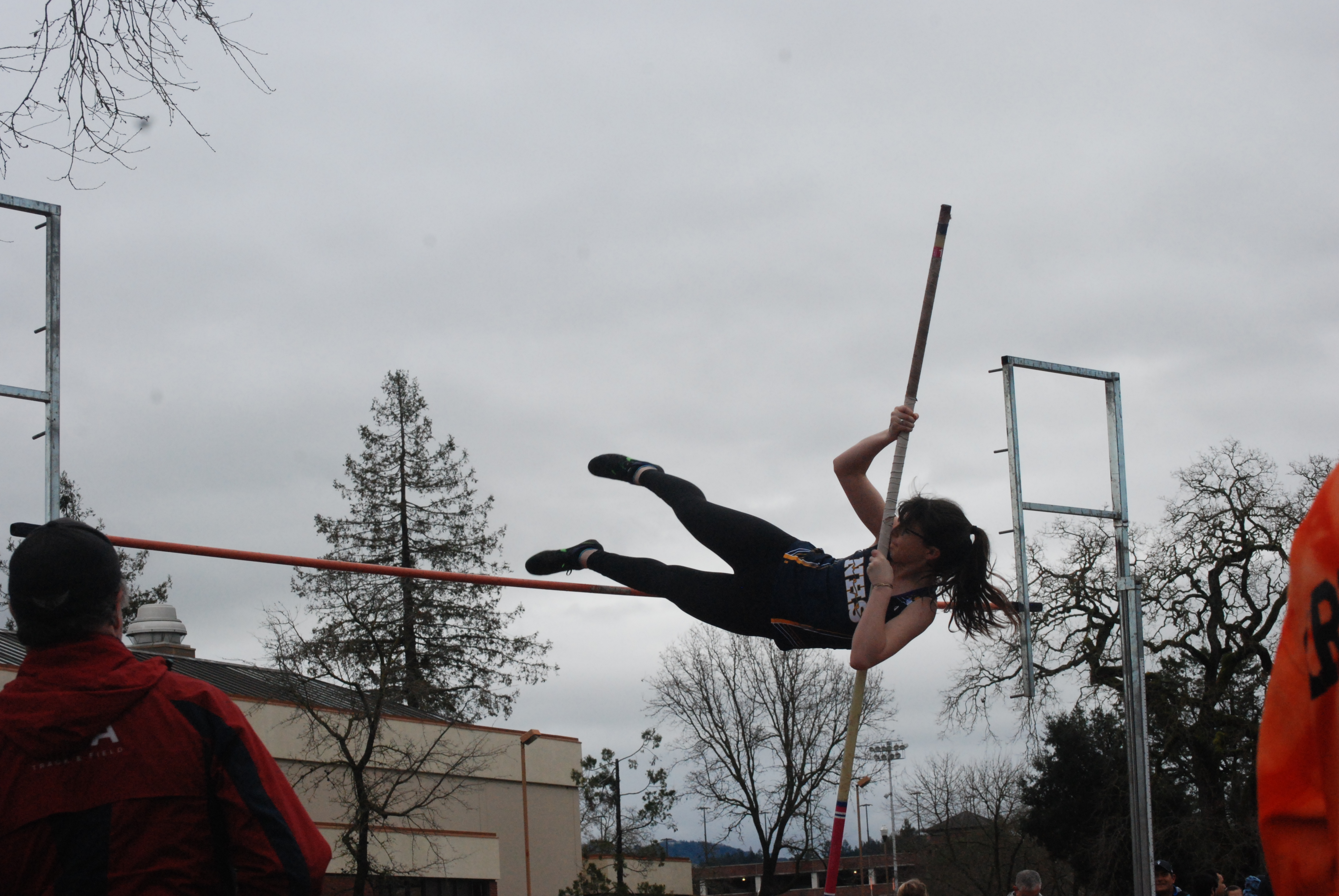 Athlete prepares for pole vault on a track with others watching.
