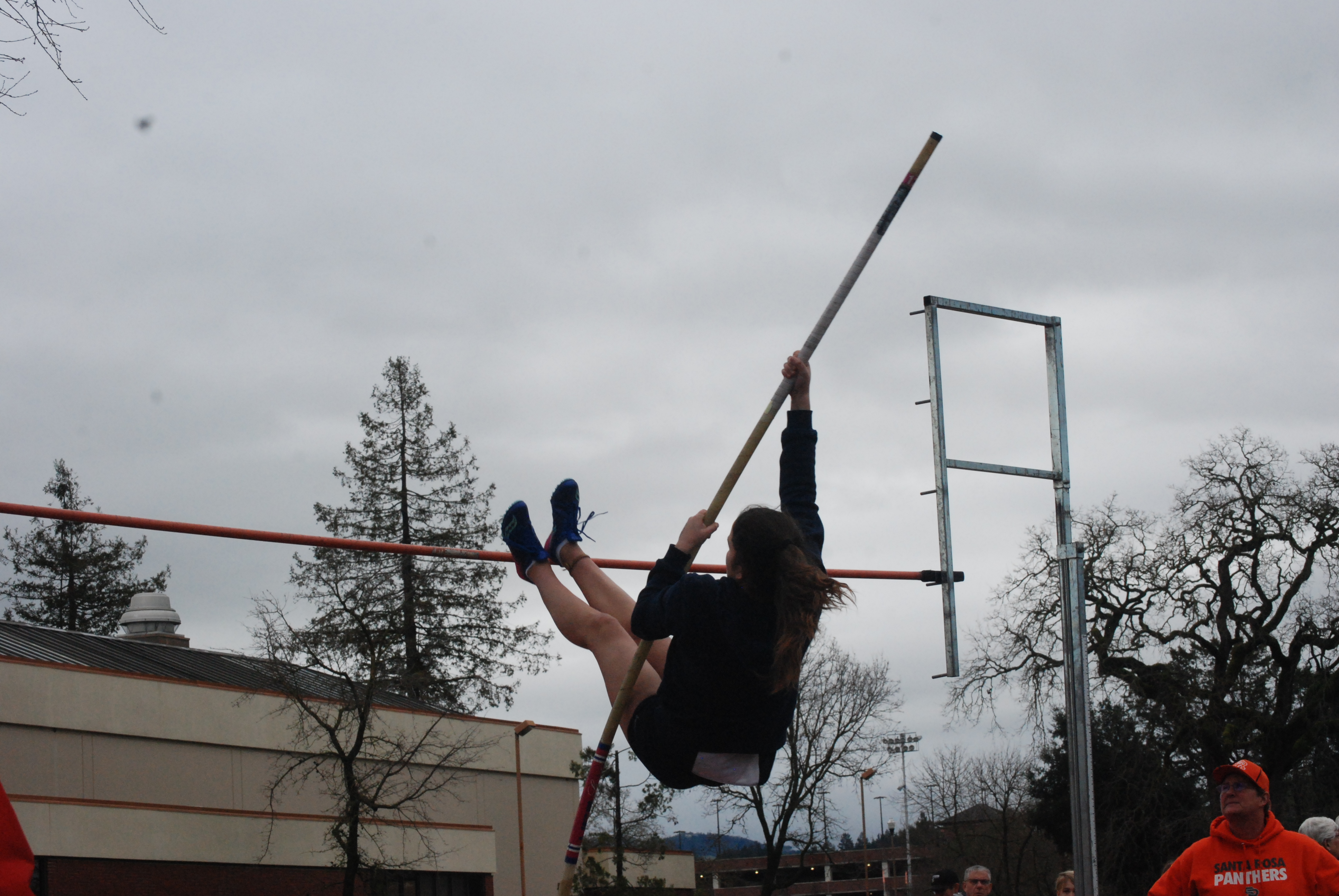 Athlete prepares for pole vault on a track with others watching.