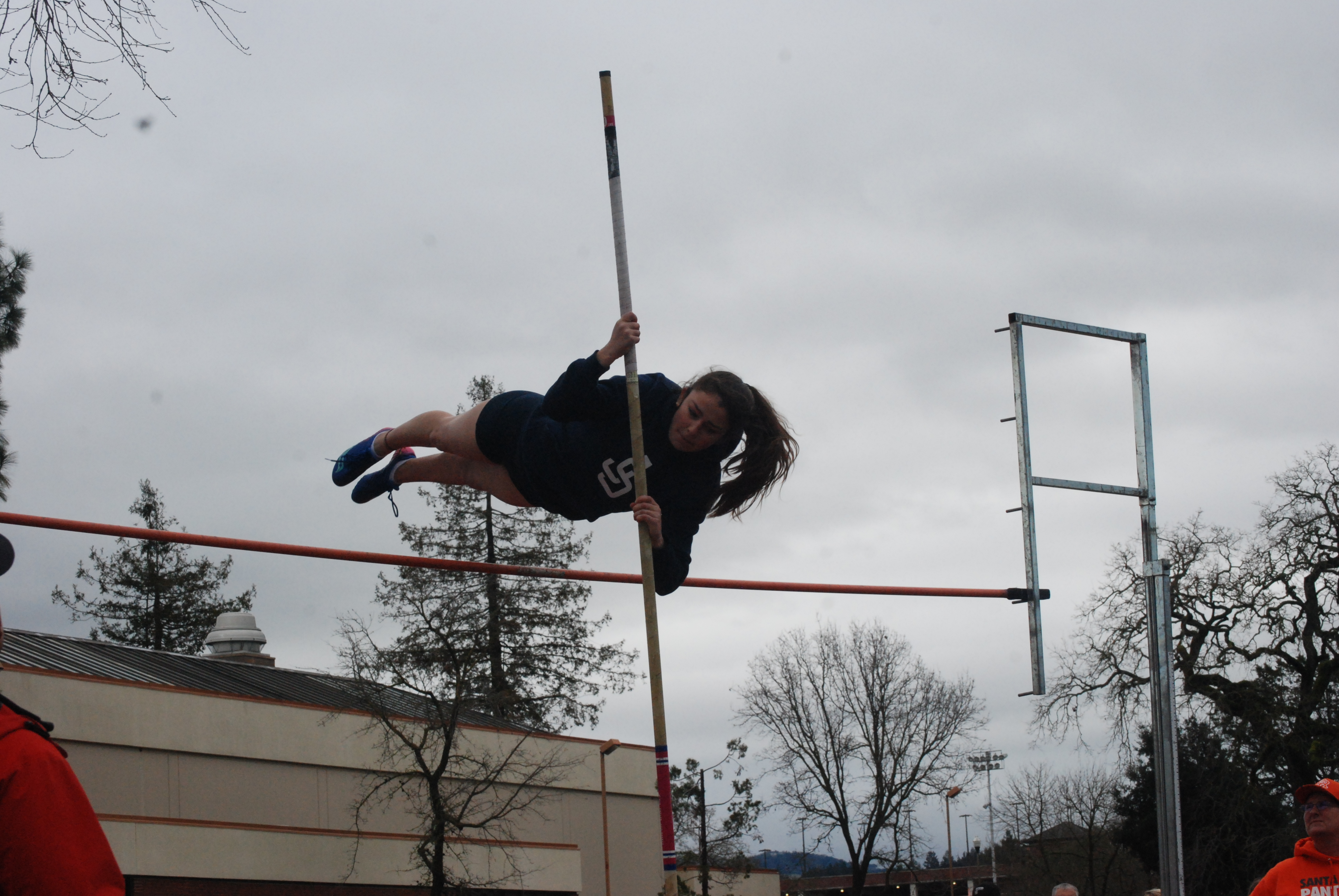 Athlete prepares for pole vault on a track with others watching.