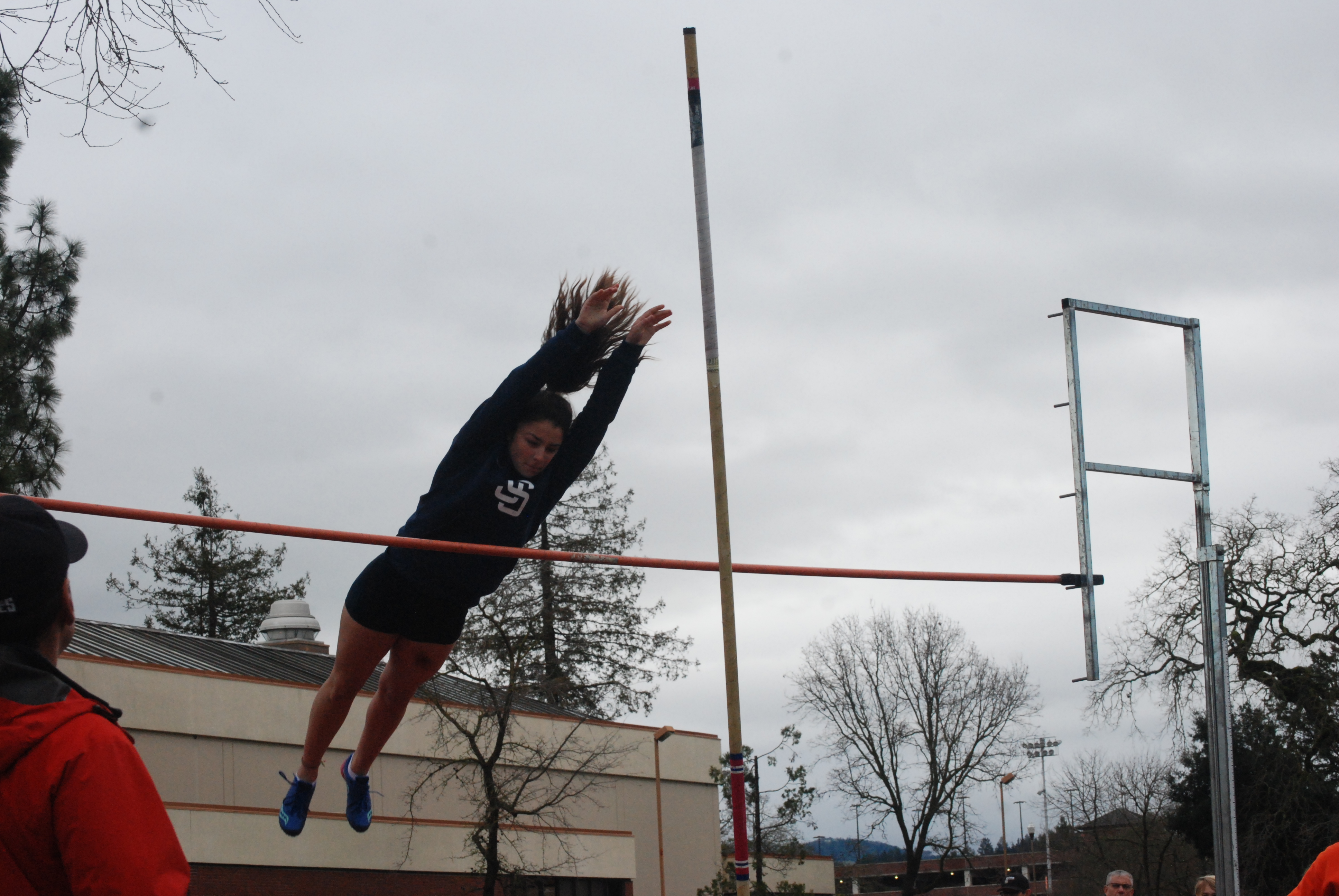Athlete prepares for pole vault on a track with others watching.
