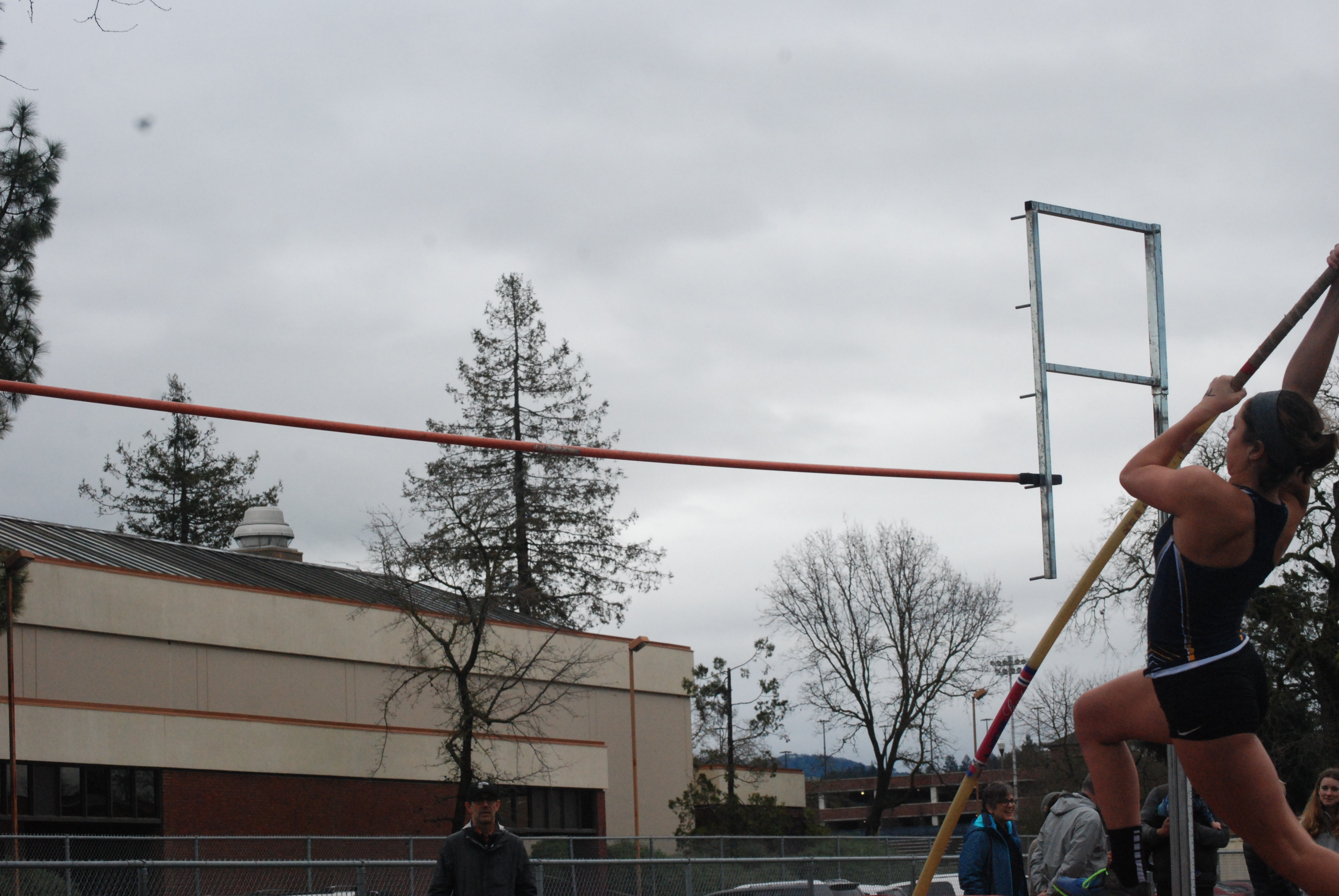 Athlete prepares for pole vault on a track with others watching.