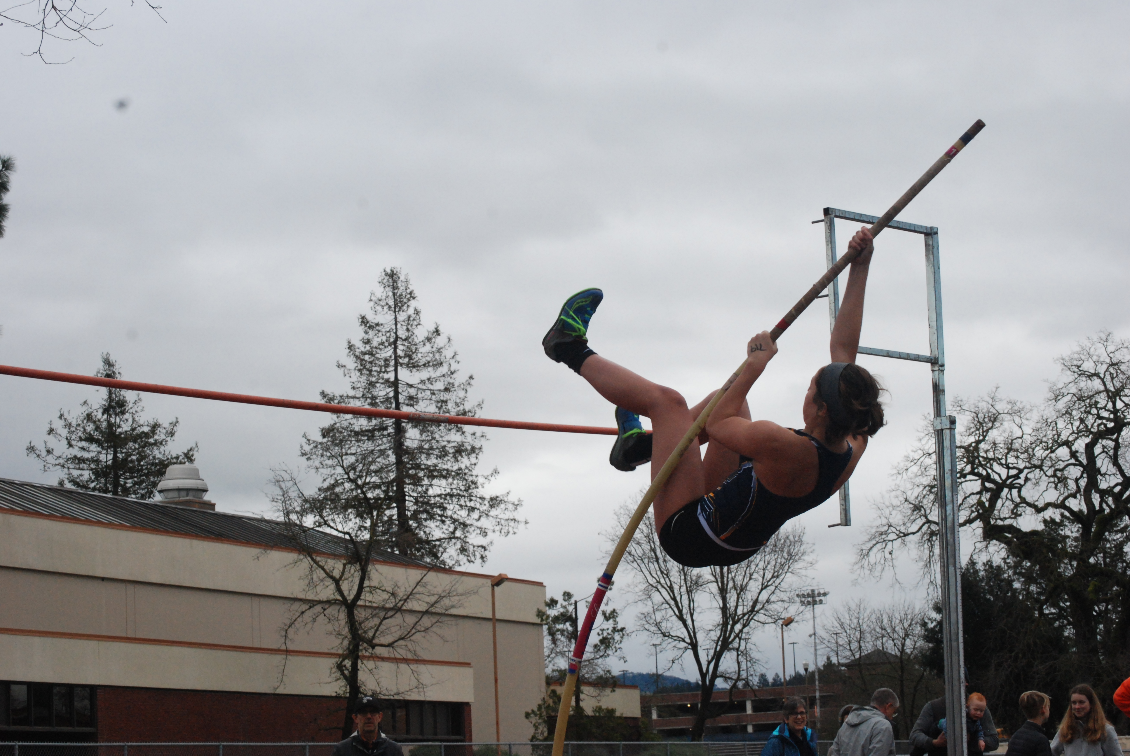Athlete prepares for pole vault on a track with others watching.