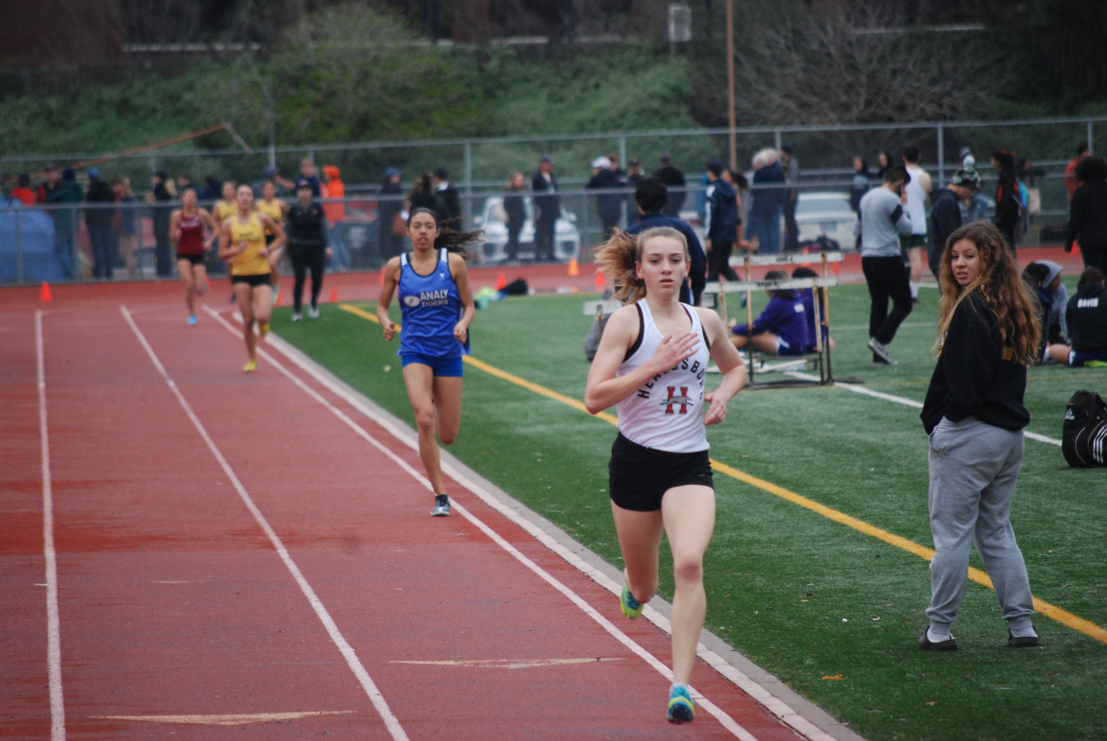 Athlete prepares for pole vault on a track with others watching.