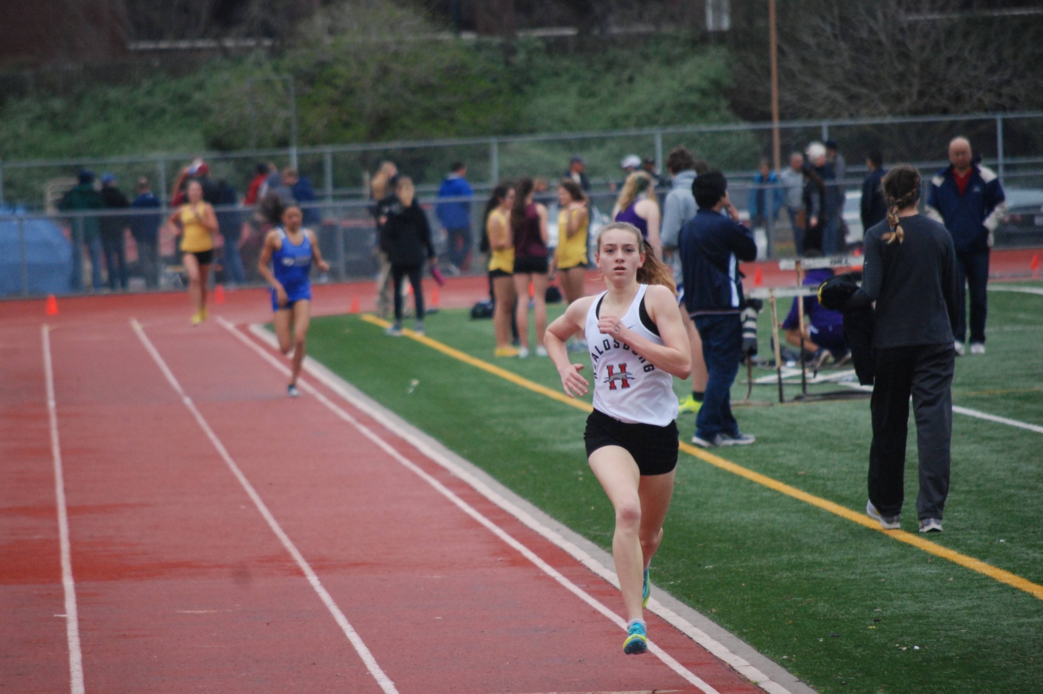 Athlete prepares for pole vault on a track with others watching.