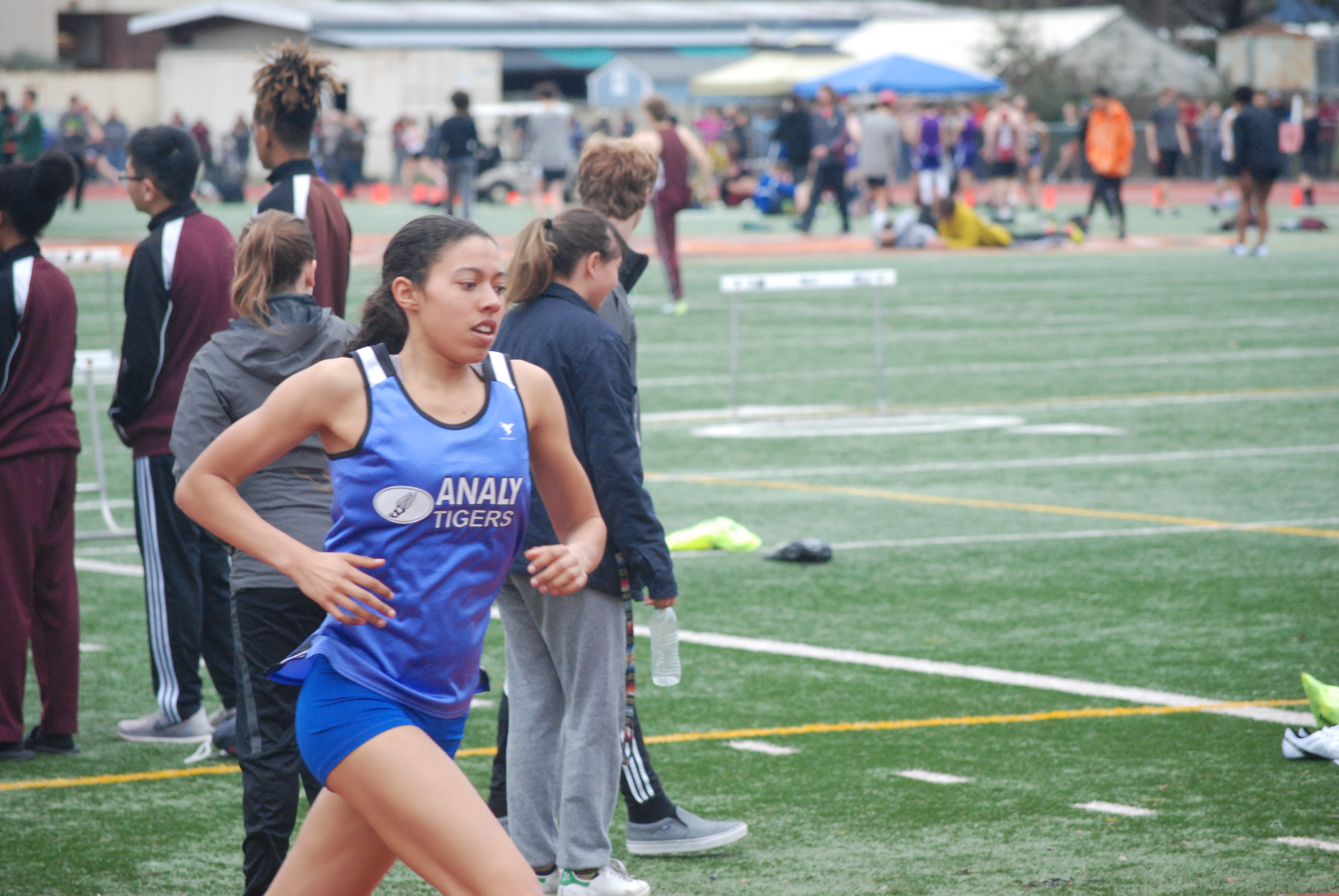 Athlete prepares for pole vault on a track with others watching.