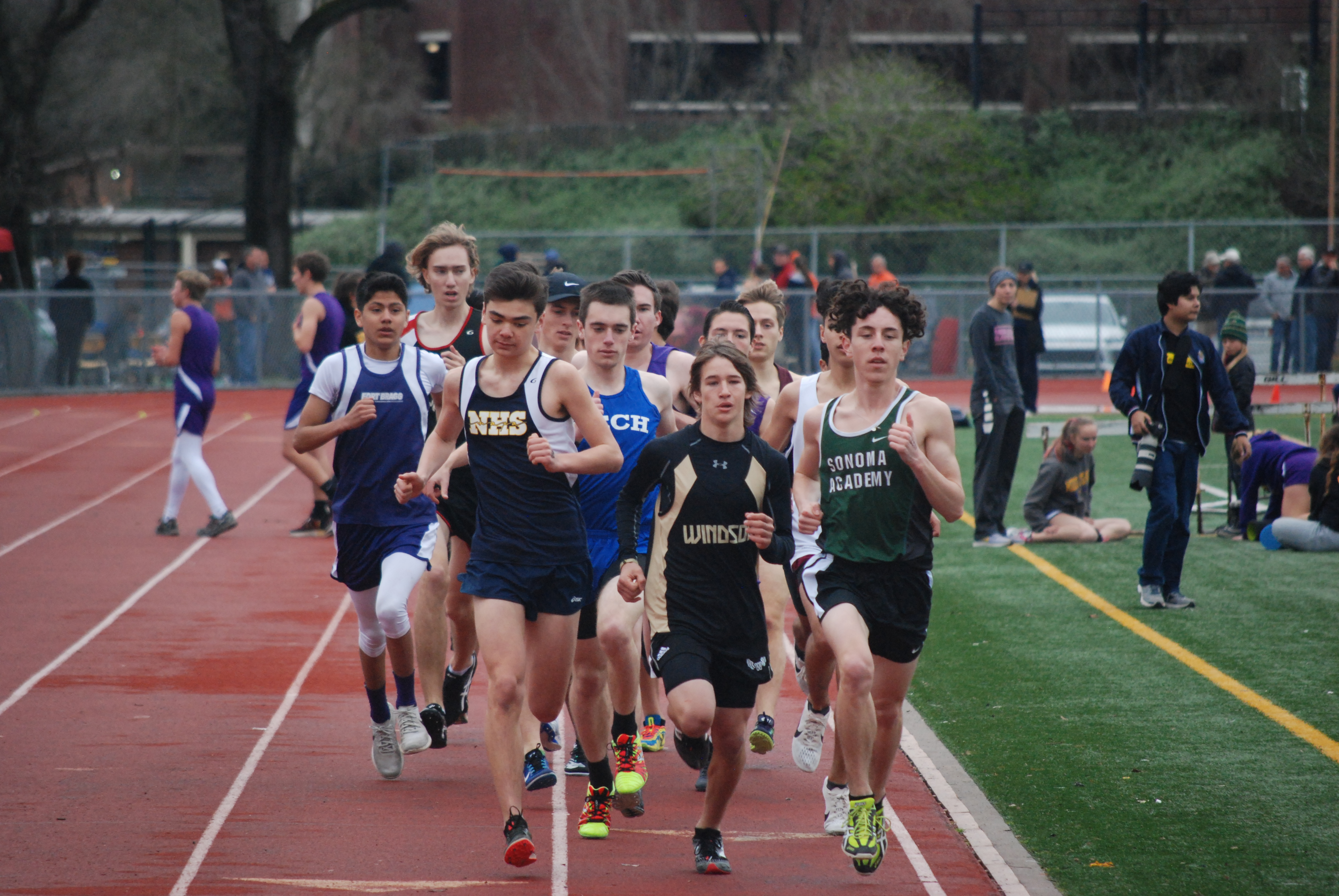 Athlete prepares for pole vault on a track with others watching.