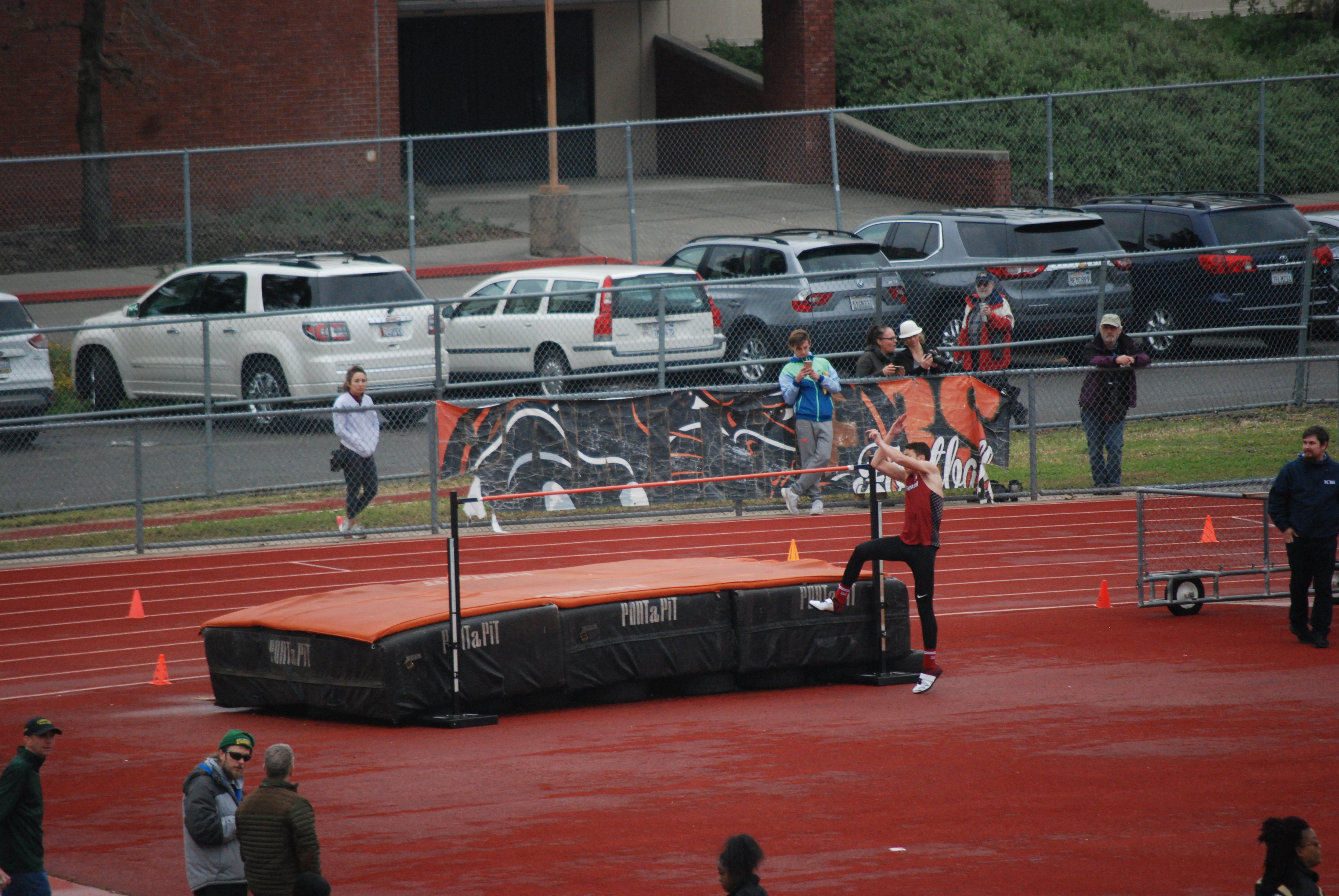 Athlete prepares for pole vault on a track with others watching.