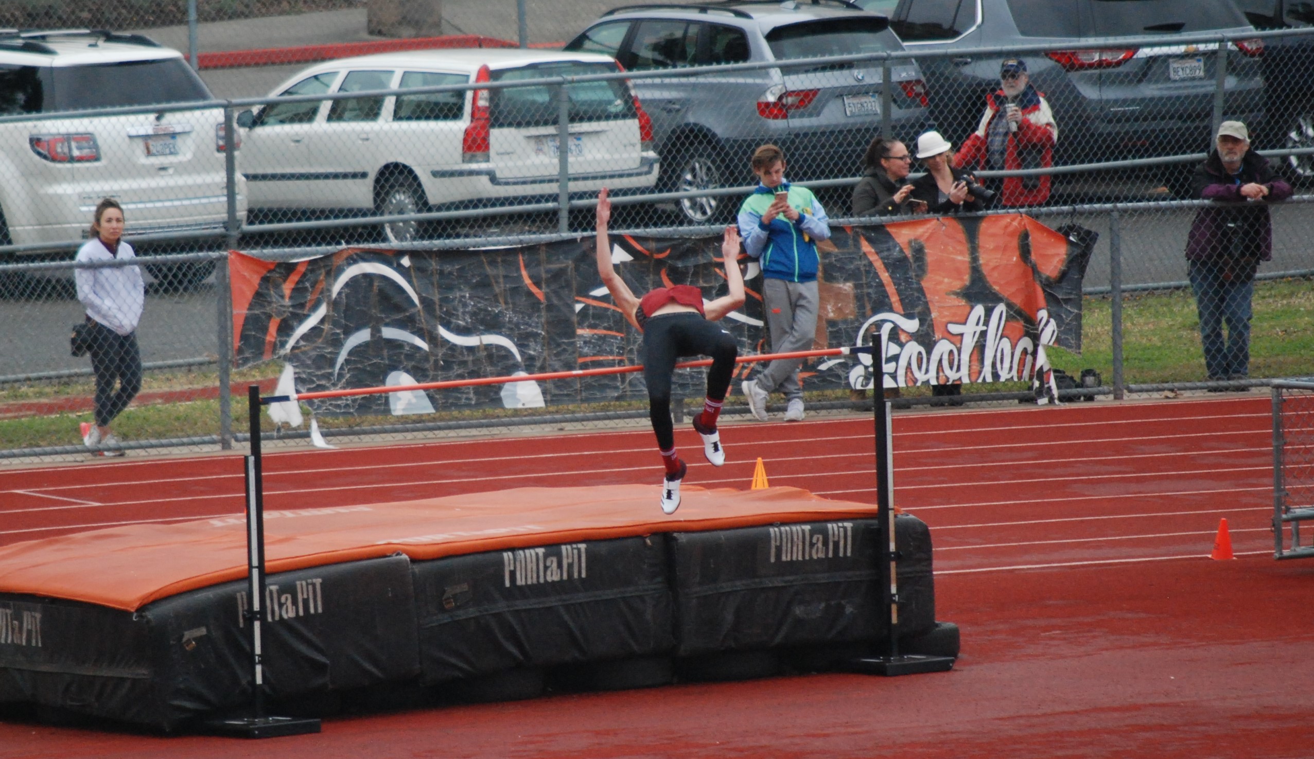 Athlete prepares for pole vault on a track with others watching.