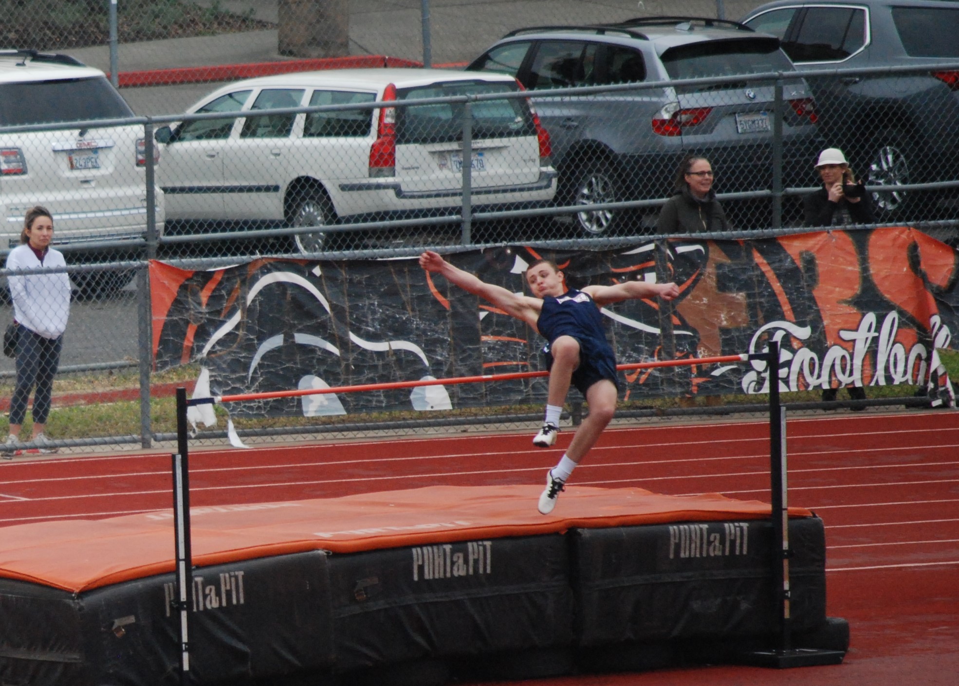 Athlete prepares for pole vault on a track with others watching.