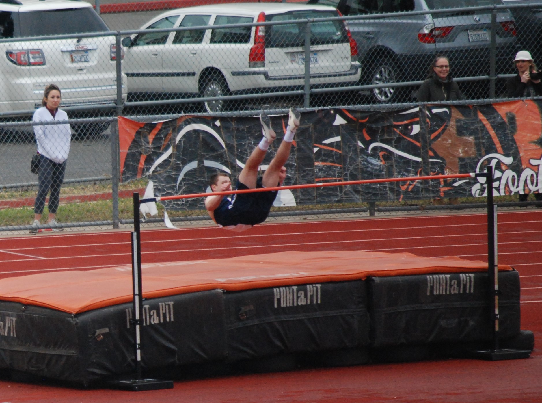 Athlete prepares for pole vault on a track with others watching.