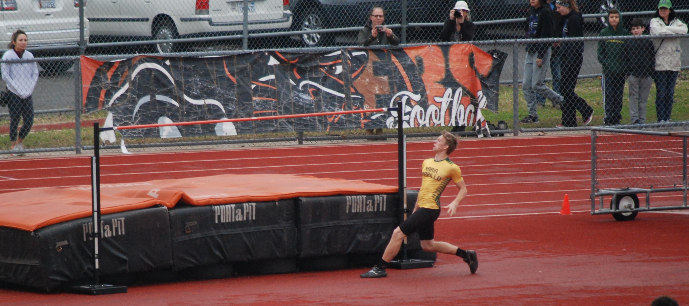 Athlete prepares for pole vault on a track with others watching.