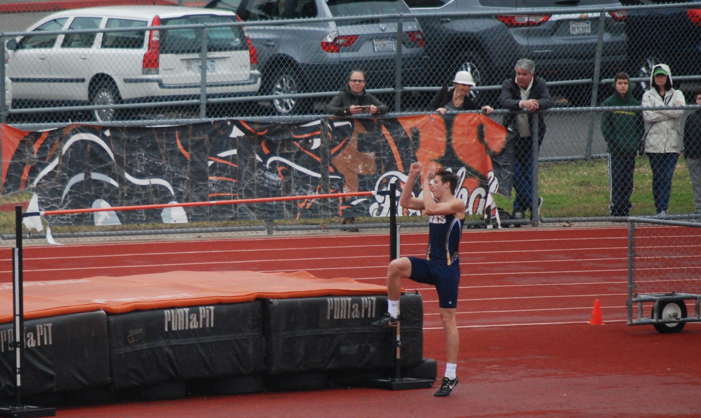 Athlete prepares for pole vault on a track with others watching.