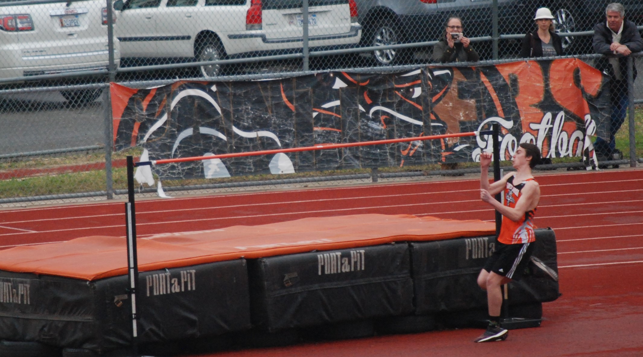 Athlete prepares for pole vault on a track with others watching.