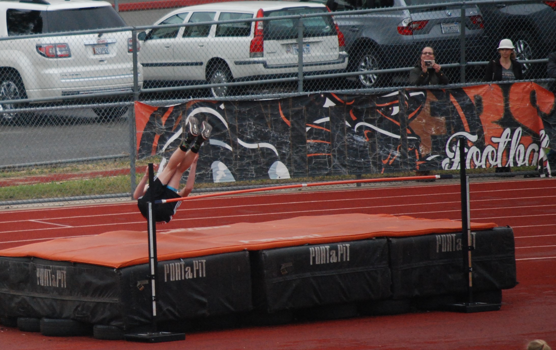 Athlete prepares for pole vault on a track with others watching.
