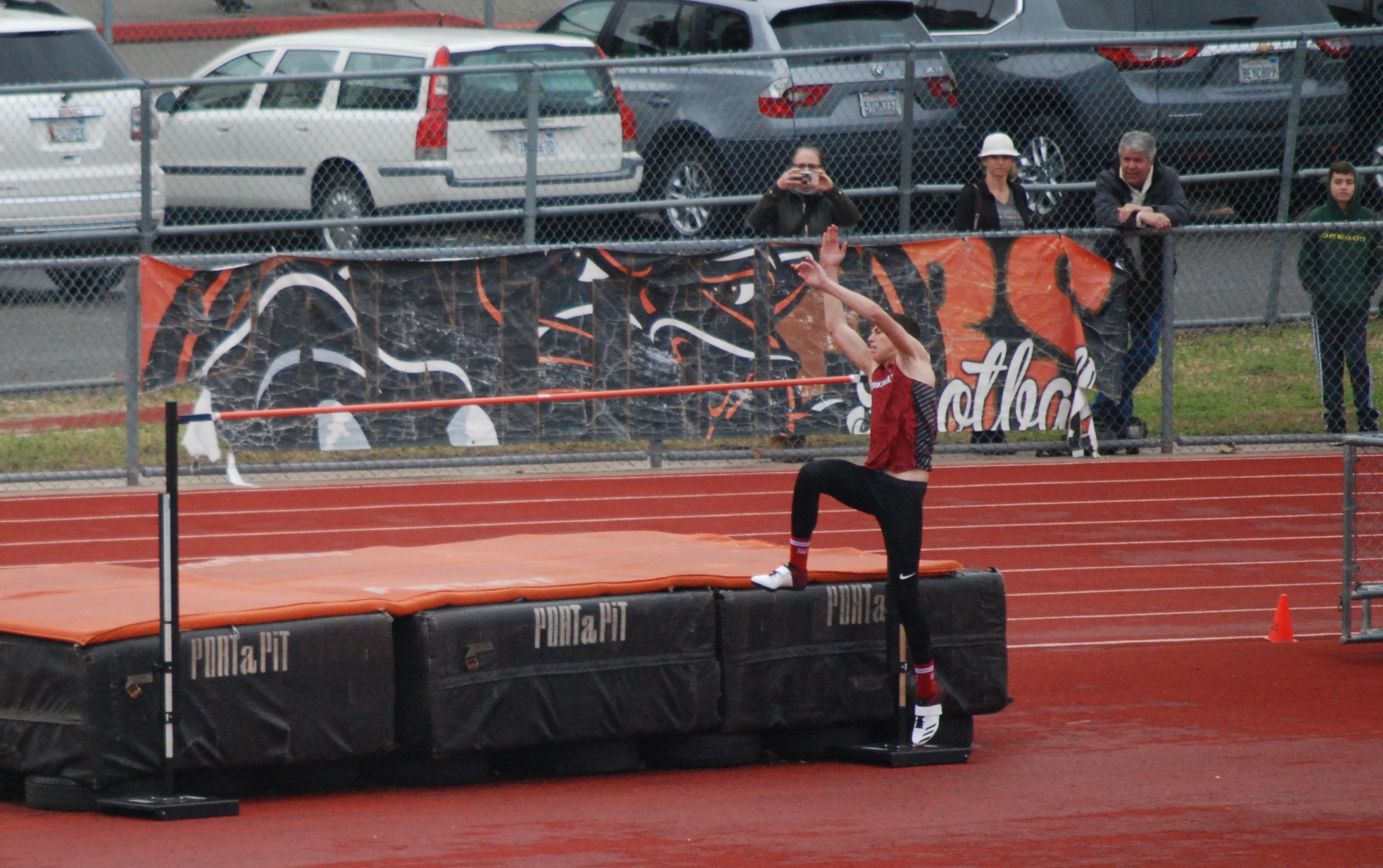 Athlete prepares for pole vault on a track with others watching.