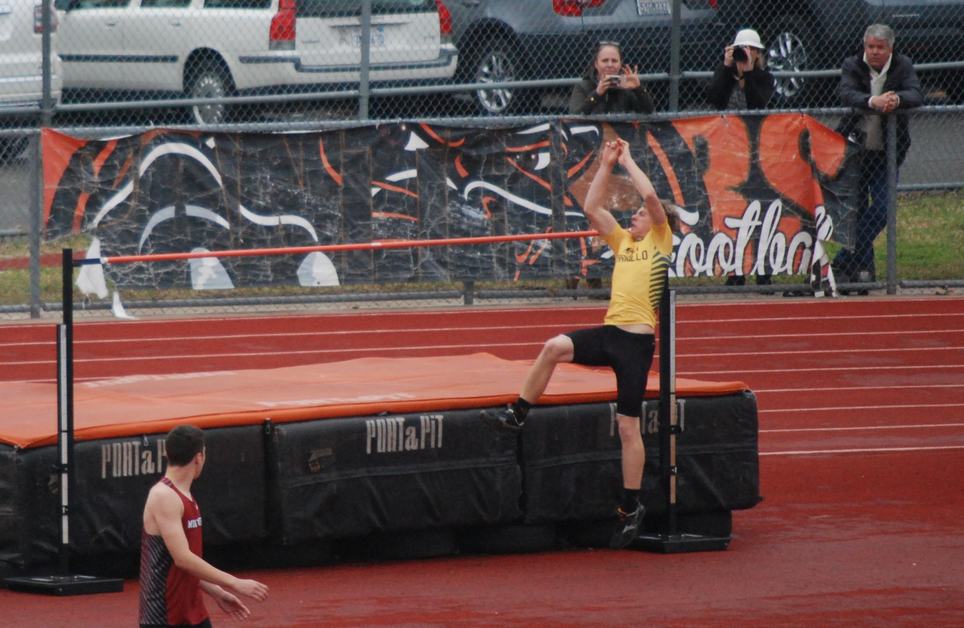 Athlete prepares for pole vault on a track with others watching.
