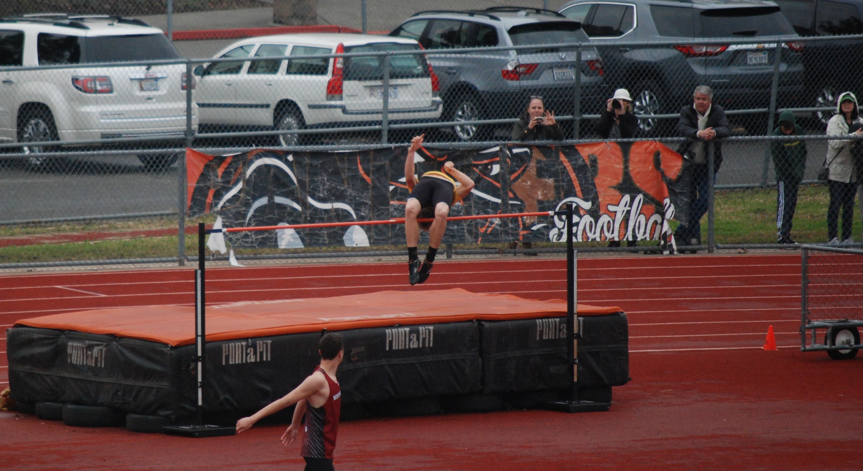 Athlete prepares for pole vault on a track with others watching.