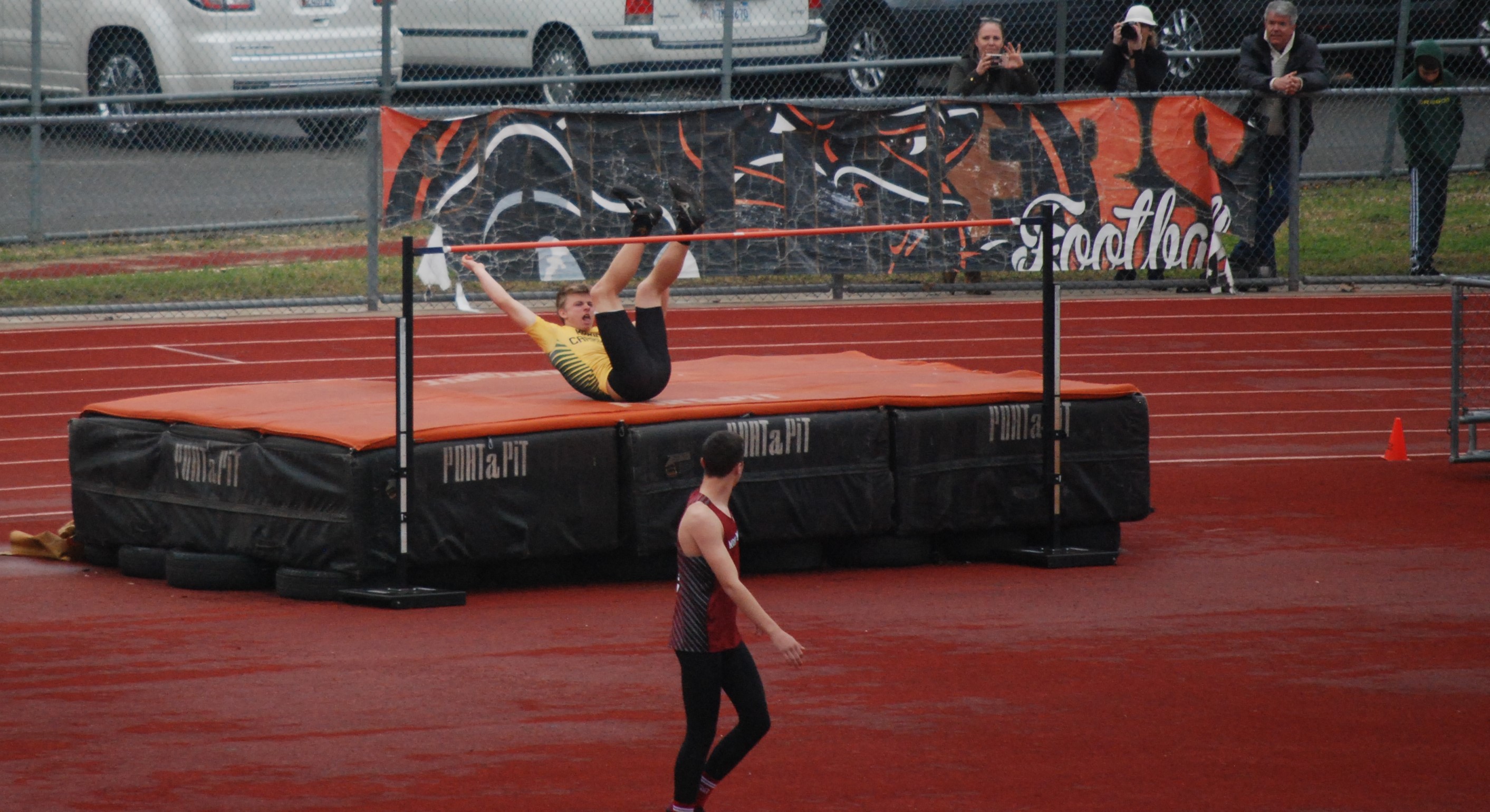 Athlete prepares for pole vault on a track with others watching.