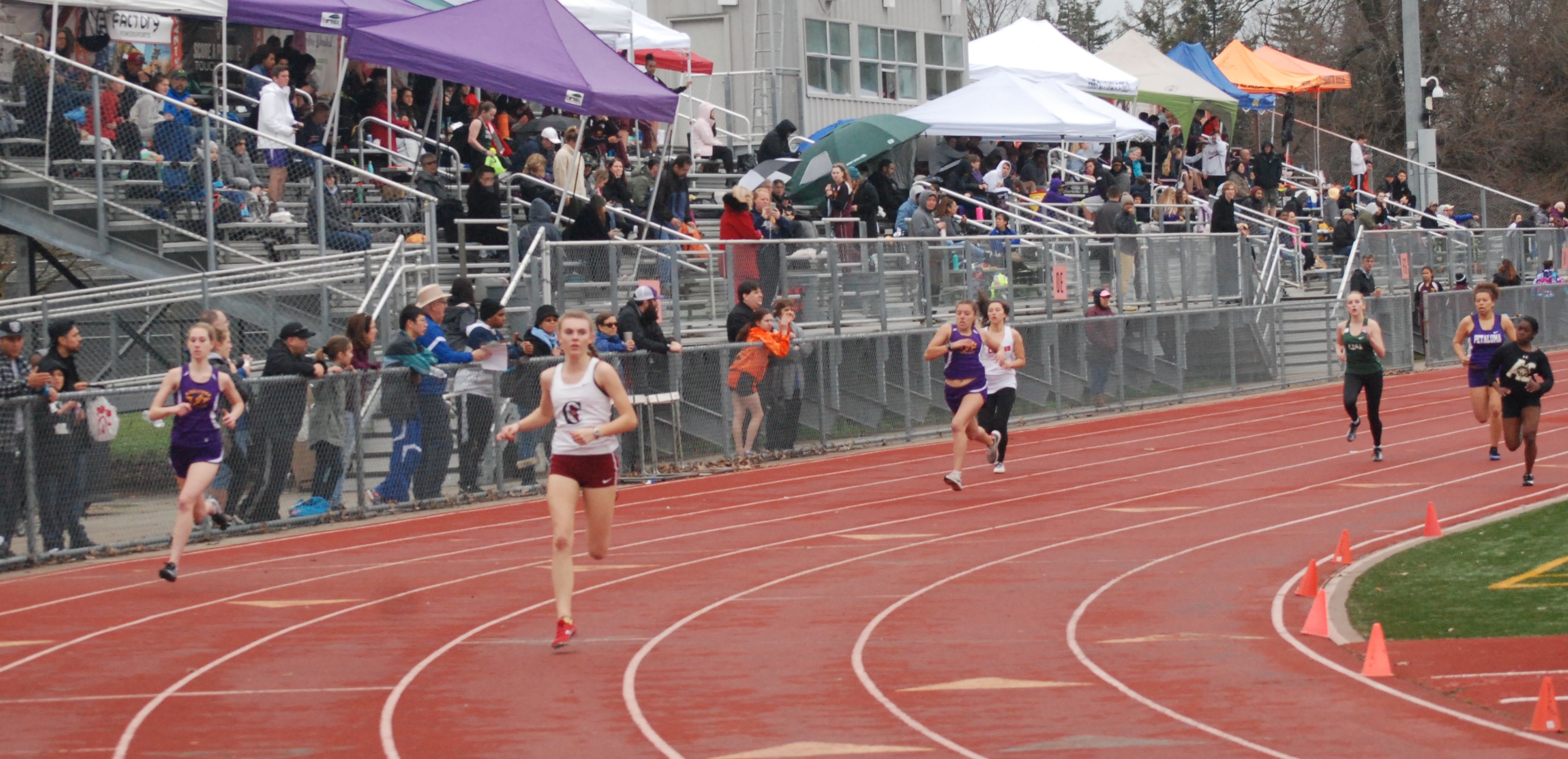 Athlete prepares for pole vault on a track with others watching.