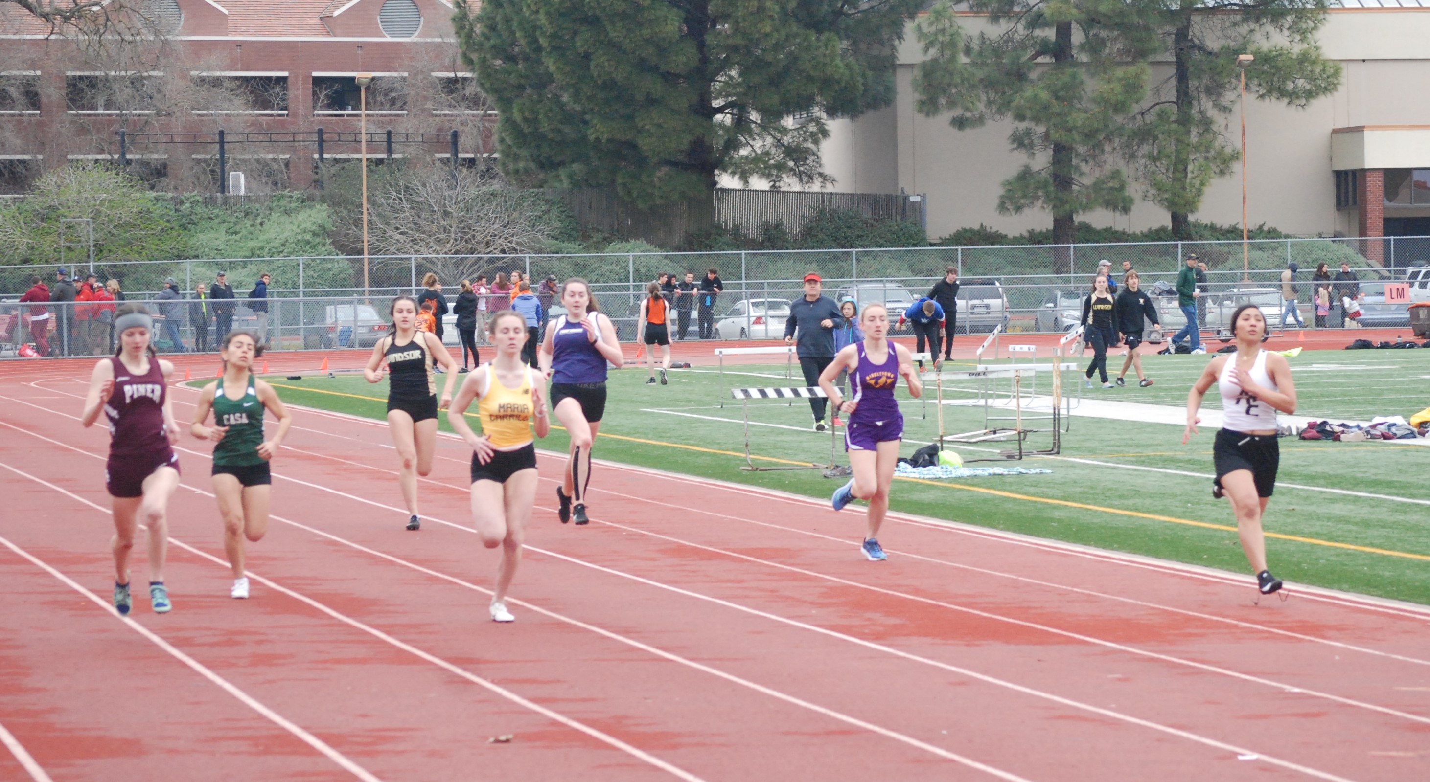 Athlete prepares for pole vault on a track with others watching.