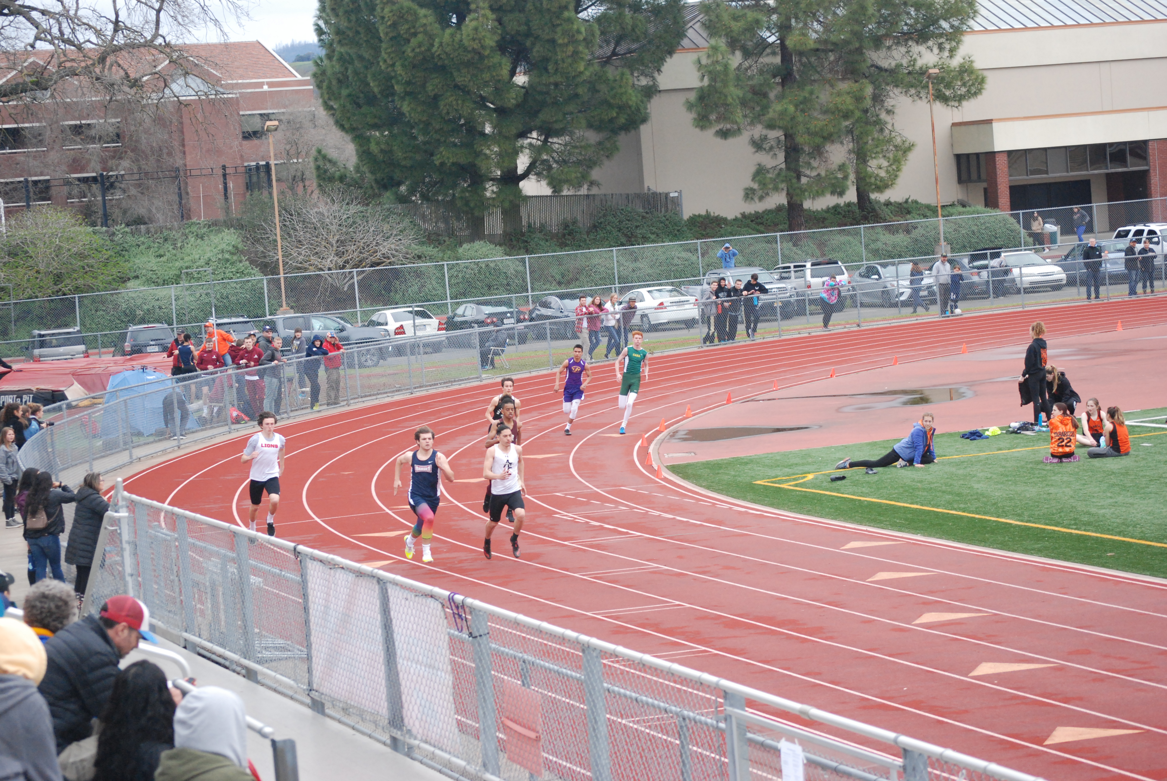 Athlete prepares for pole vault on a track with others watching.